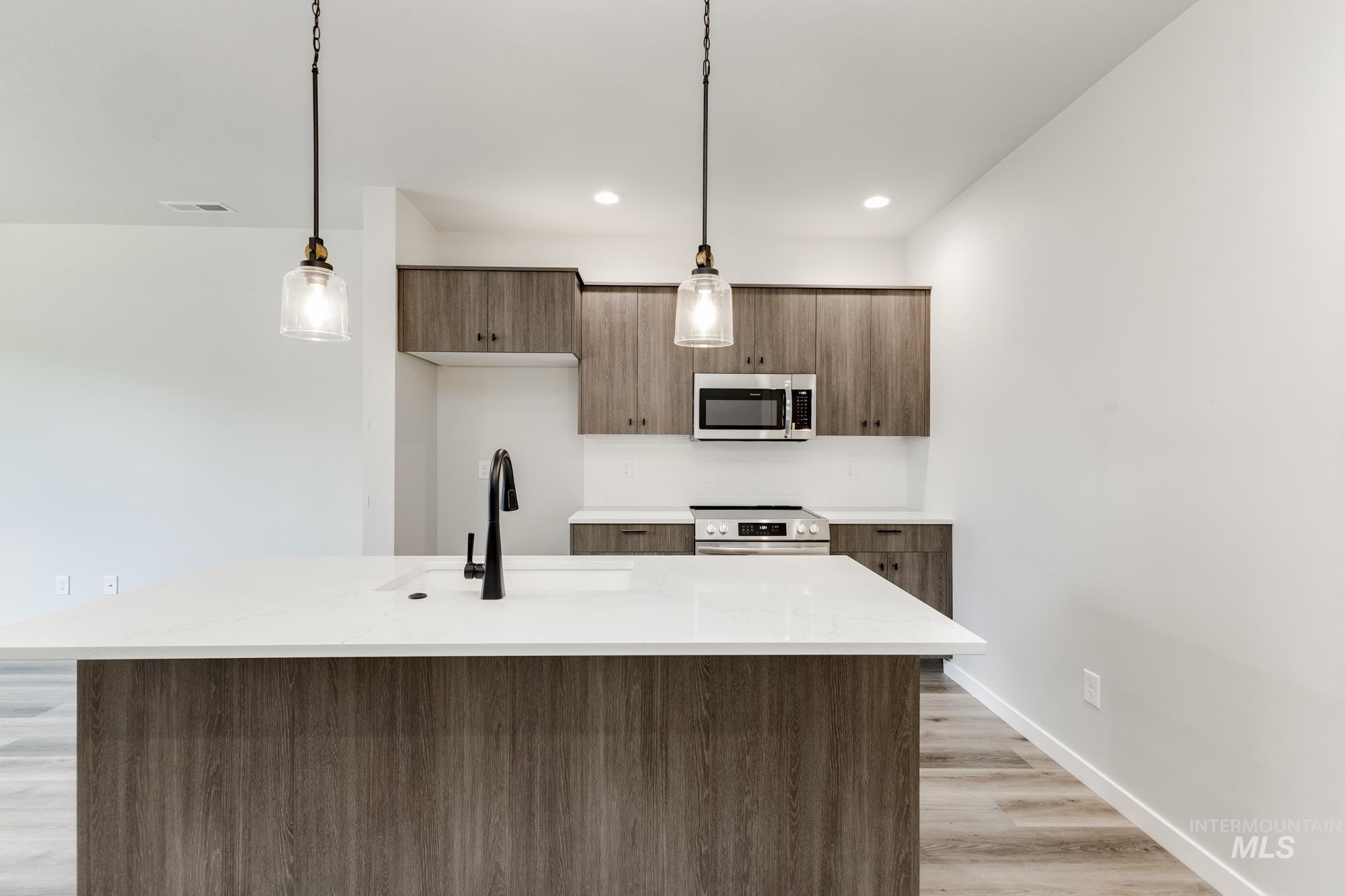 Kitchen featuring pendant lighting, modern cabinets, light stone counters, stainless steel appliances, and light wood-type flooring