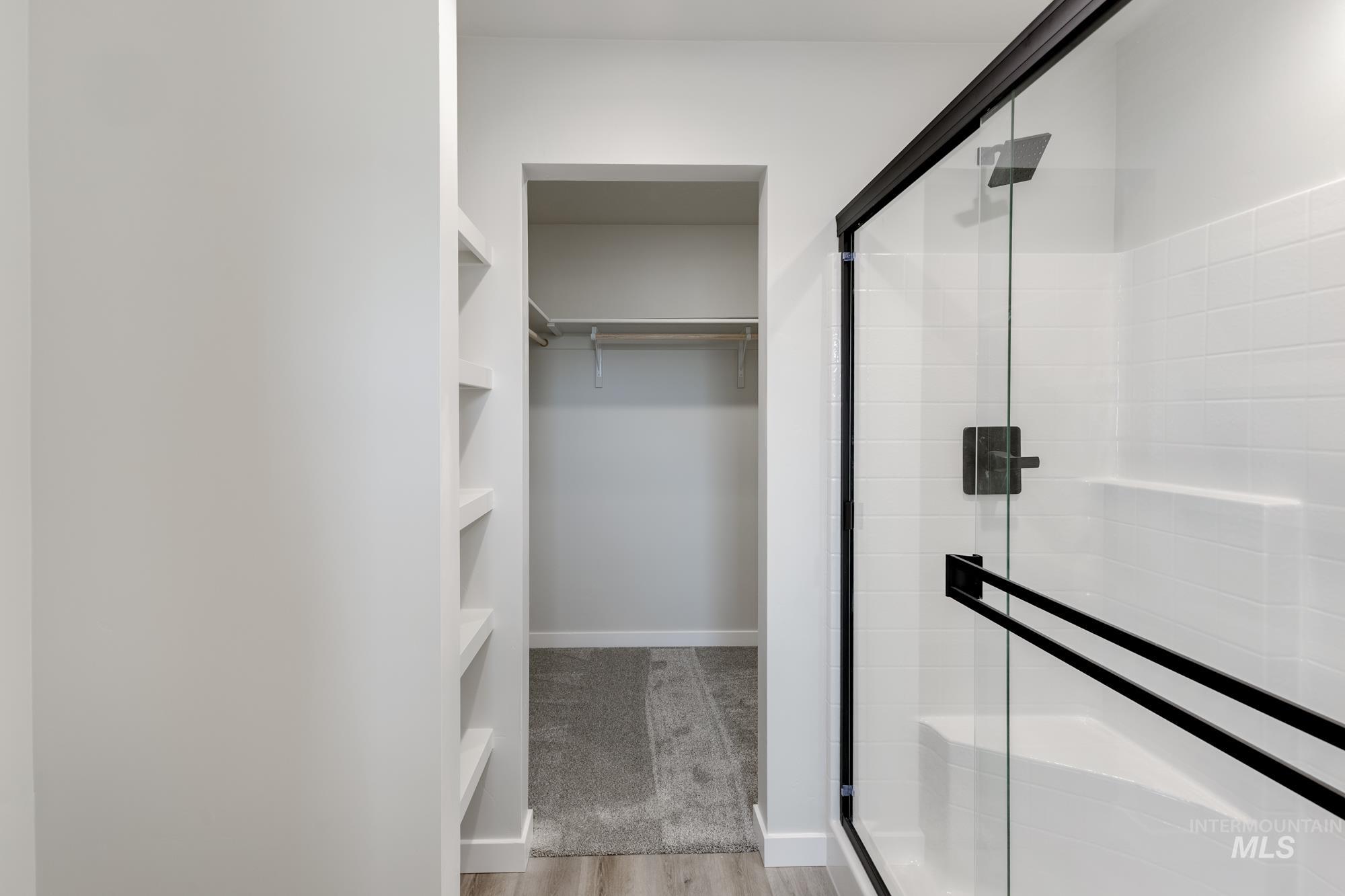 Bathroom with a spacious closet, a stall shower, and light wood-style flooring