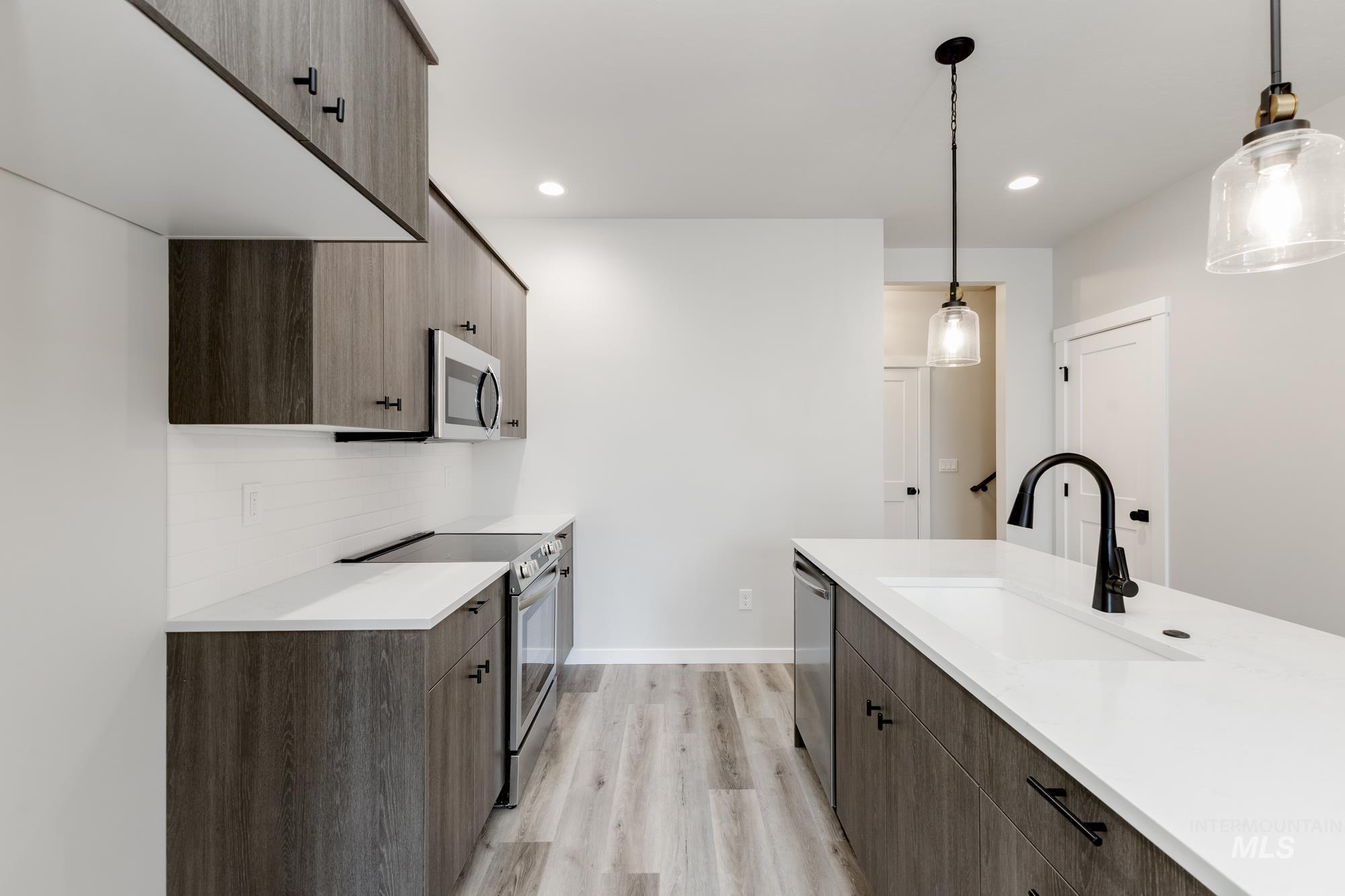Kitchen featuring modern cabinets, appliances with stainless steel finishes, light wood finished floors, hanging light fixtures, and recessed lighting