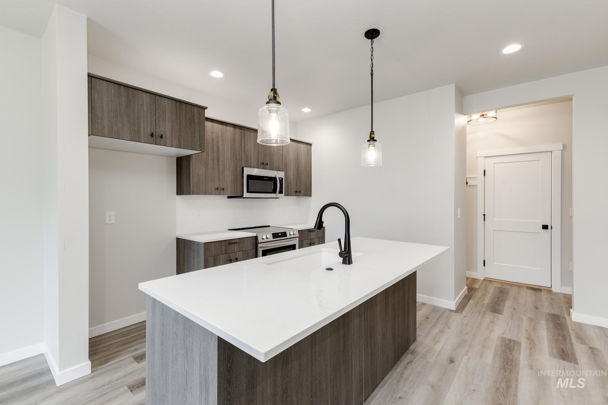 Kitchen featuring modern cabinets, hanging light fixtures, a center island with sink, stainless steel appliances, and light wood-type flooring