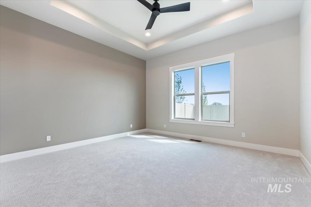 Empty room with a tray ceiling, light carpet, a ceiling fan, and recessed lighting