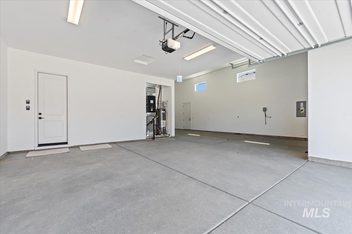 Garage with electric panel, gas water heater, and a garage door opener