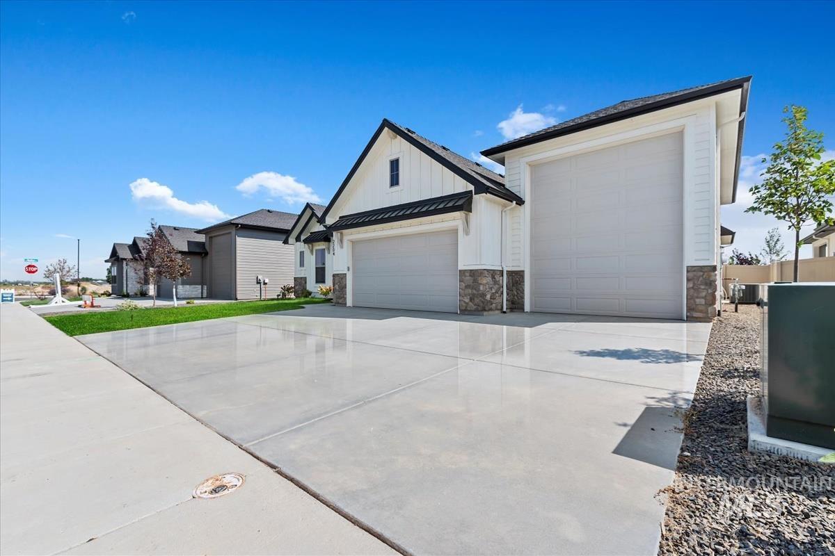 View of front of property featuring driveway, a garage, stone siding, board and batten siding, and a metal roof
