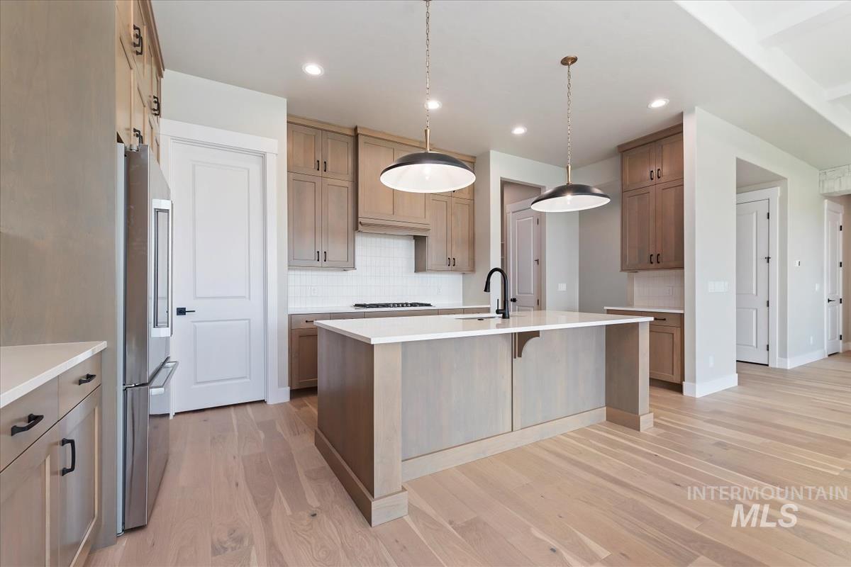 Kitchen with a kitchen bar, backsplash, decorative light fixtures, light wood finished floors, and light stone countertops