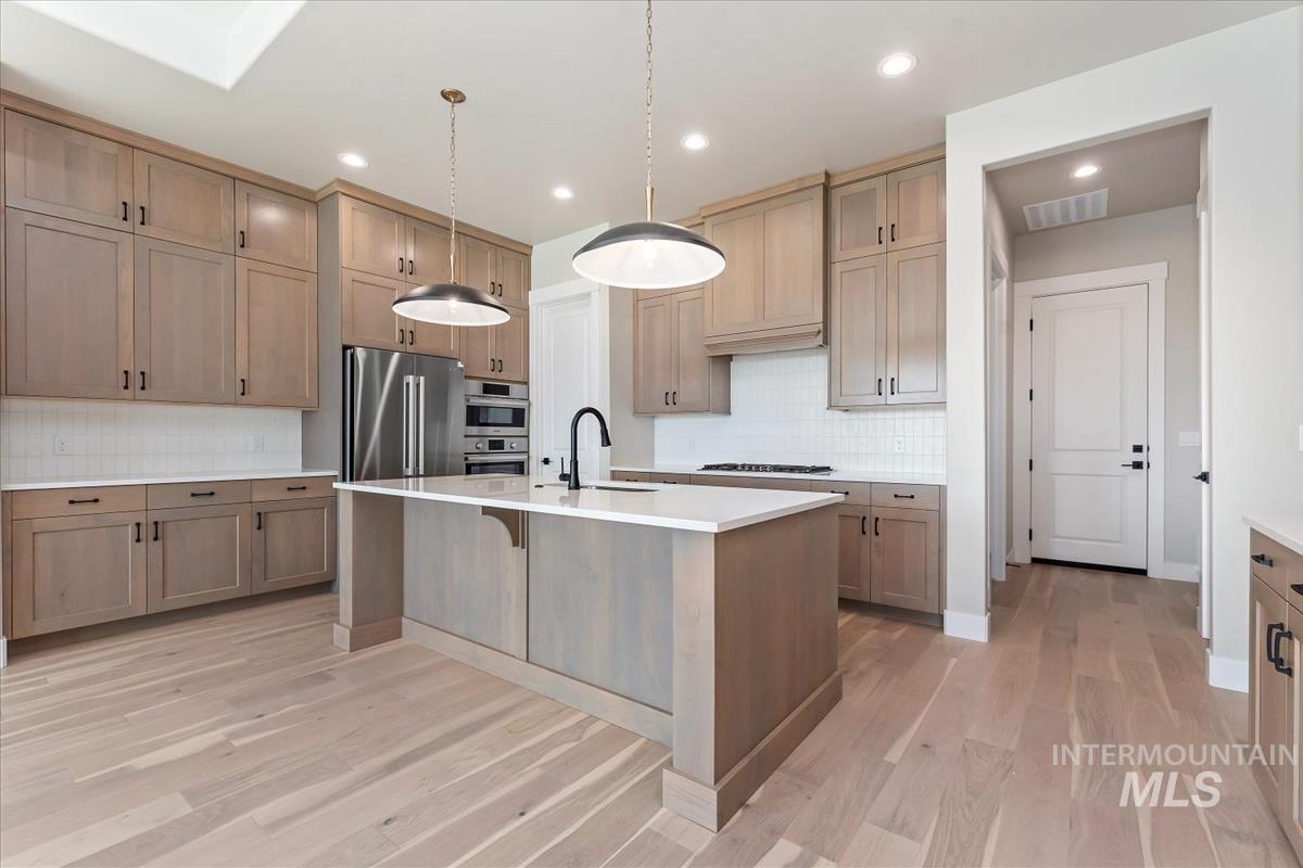Kitchen featuring a breakfast bar, a kitchen island with sink, decorative light fixtures, decorative backsplash, and stainless steel appliances