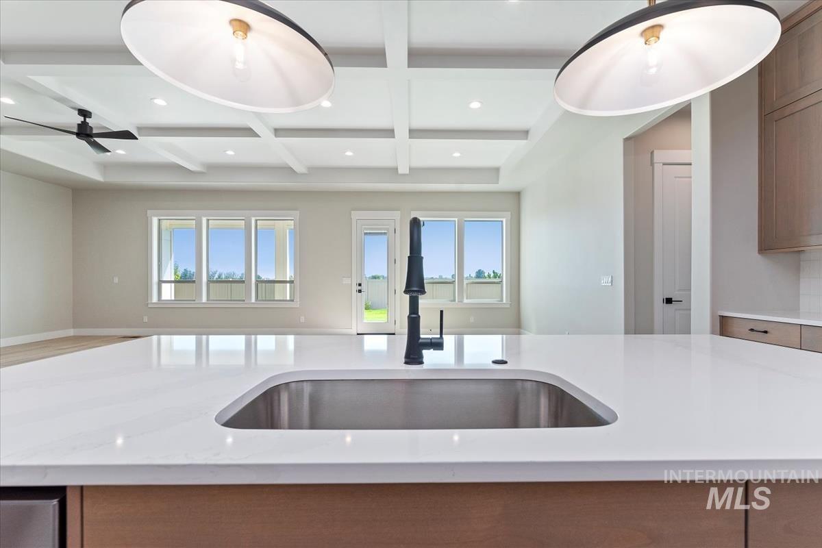 Kitchen featuring open floor plan, coffered ceiling, beamed ceiling, light stone counters, and recessed lighting