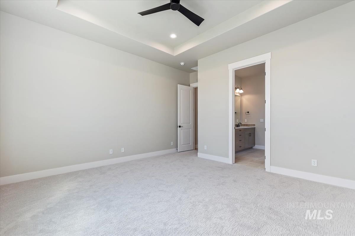 Unfurnished bedroom featuring a tray ceiling, light colored carpet, a ceiling fan, ensuite bathroom, and recessed lighting