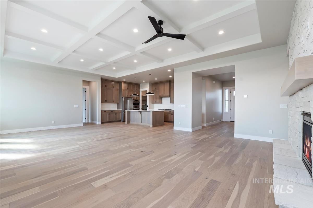 Unfurnished living room featuring beamed ceiling, a fireplace, ceiling fan, light wood finished floors, and coffered ceiling