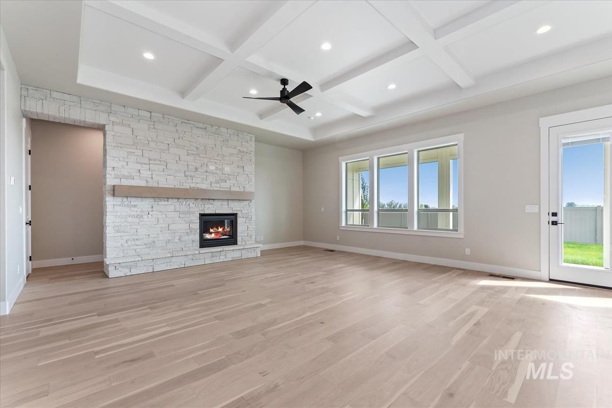 Unfurnished living room featuring light wood-style floors, ceiling fan, beam ceiling, a fireplace, and coffered ceiling