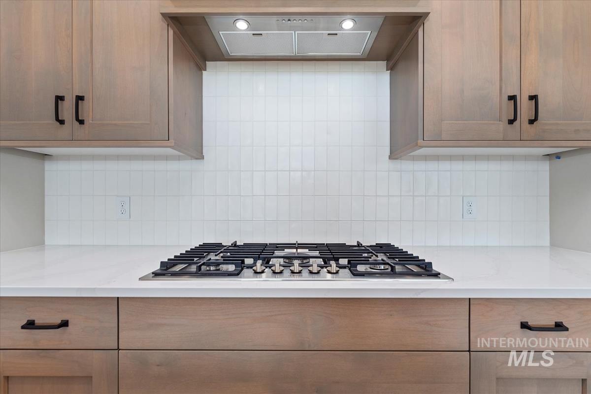 Kitchen featuring ventilation hood, stainless steel gas cooktop, backsplash, and light stone countertops
