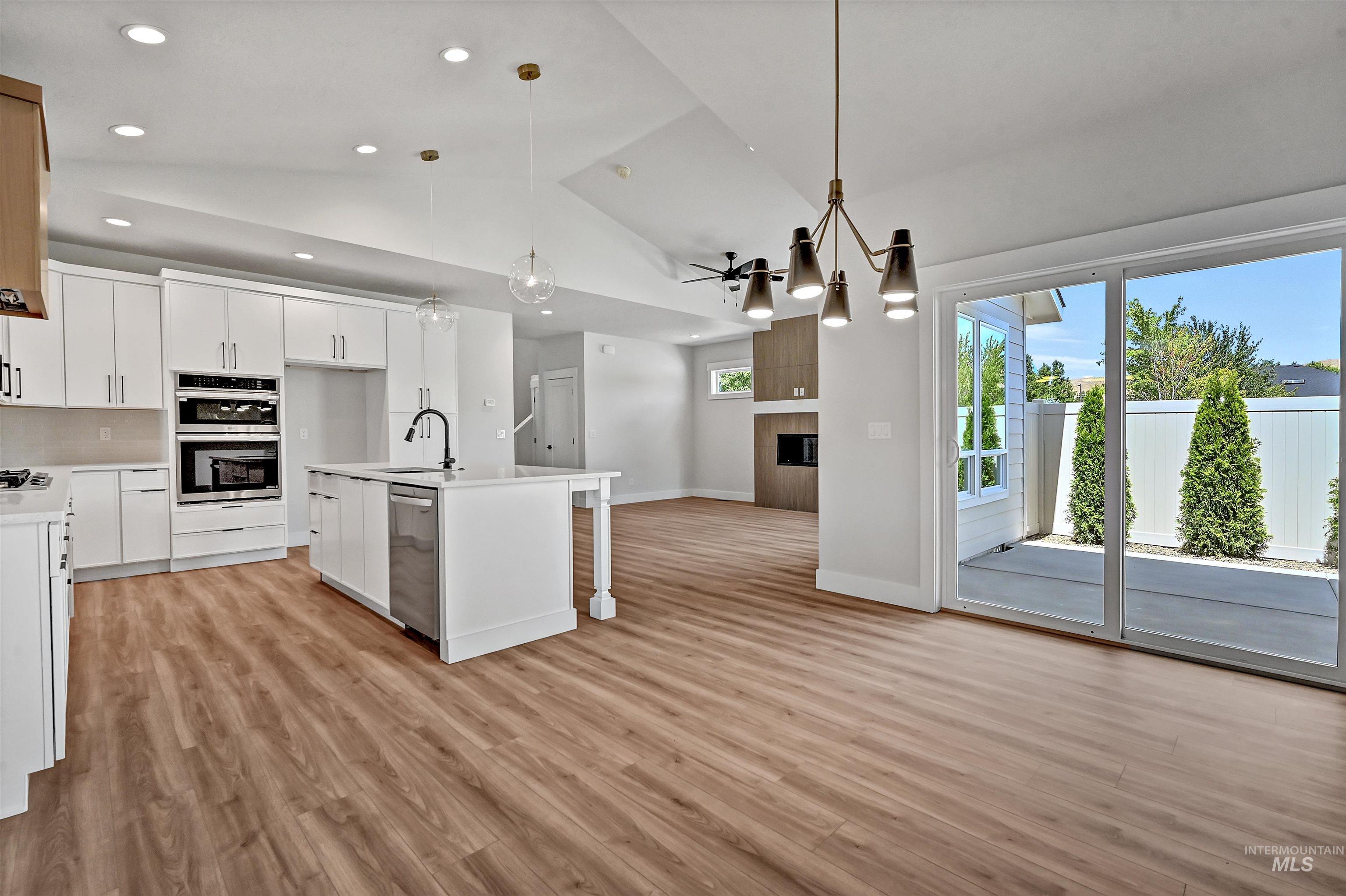 Kitchen with white cabinets, pendant lighting, a large fireplace, a kitchen island with sink, and open floor plan