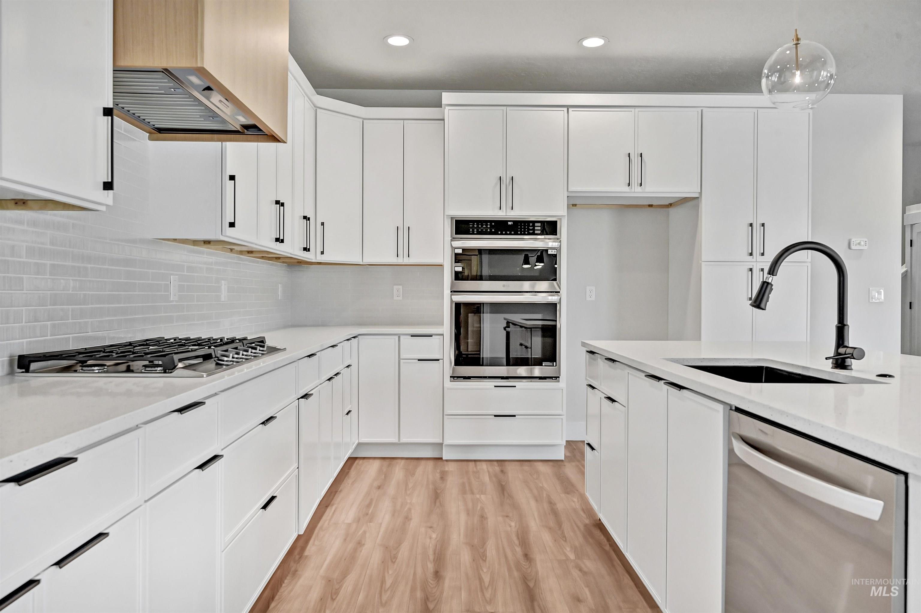 Kitchen with white cabinetry, appliances with stainless steel finishes, light stone countertops, hanging light fixtures, and recessed lighting