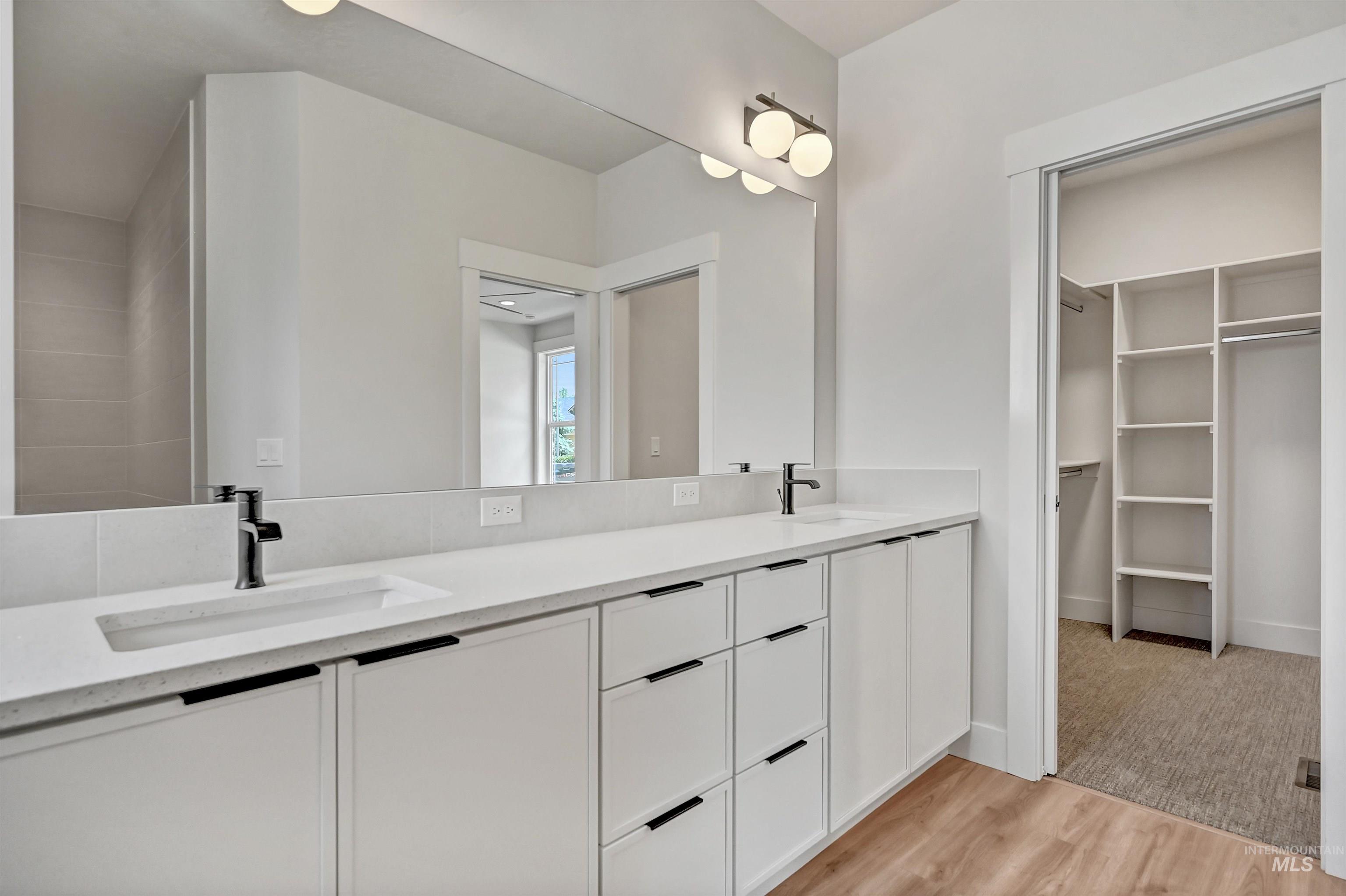 Full bath with double vanity, light wood-style flooring, and a spacious closet