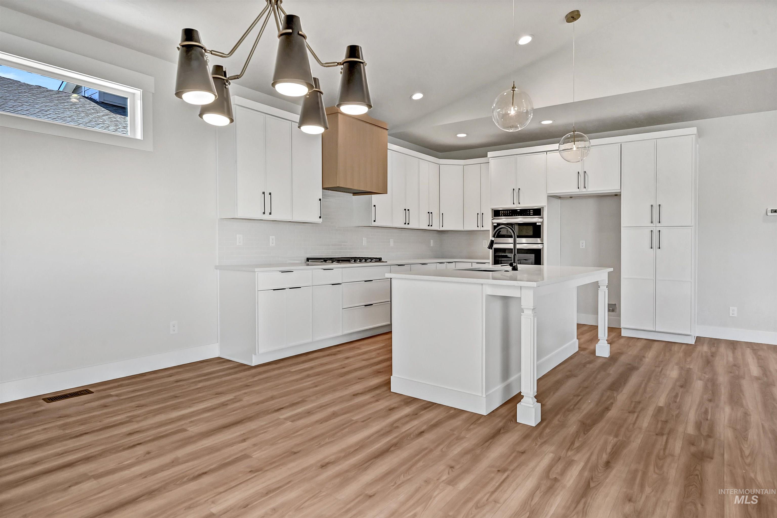 Kitchen featuring white cabinetry, lofted ceiling, hanging light fixtures, a kitchen breakfast bar, and decorative backsplash