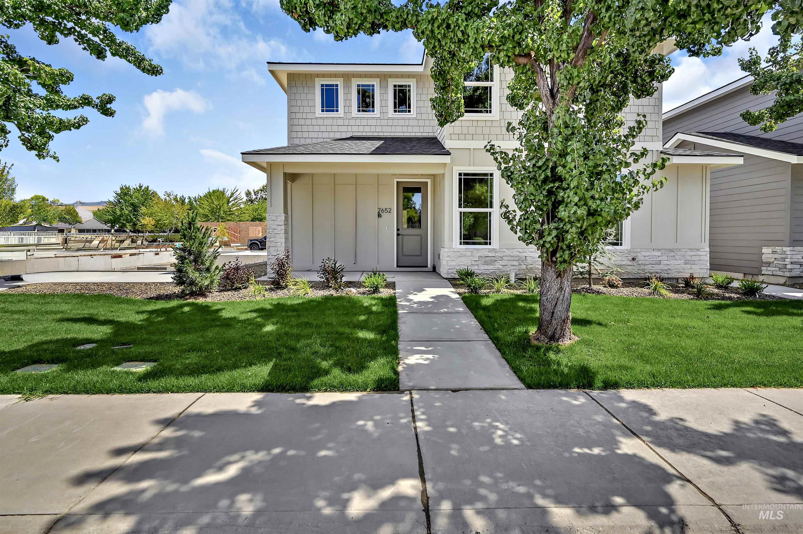 View of front of home with board and batten siding, stone siding, a front yard, and a shingled roof