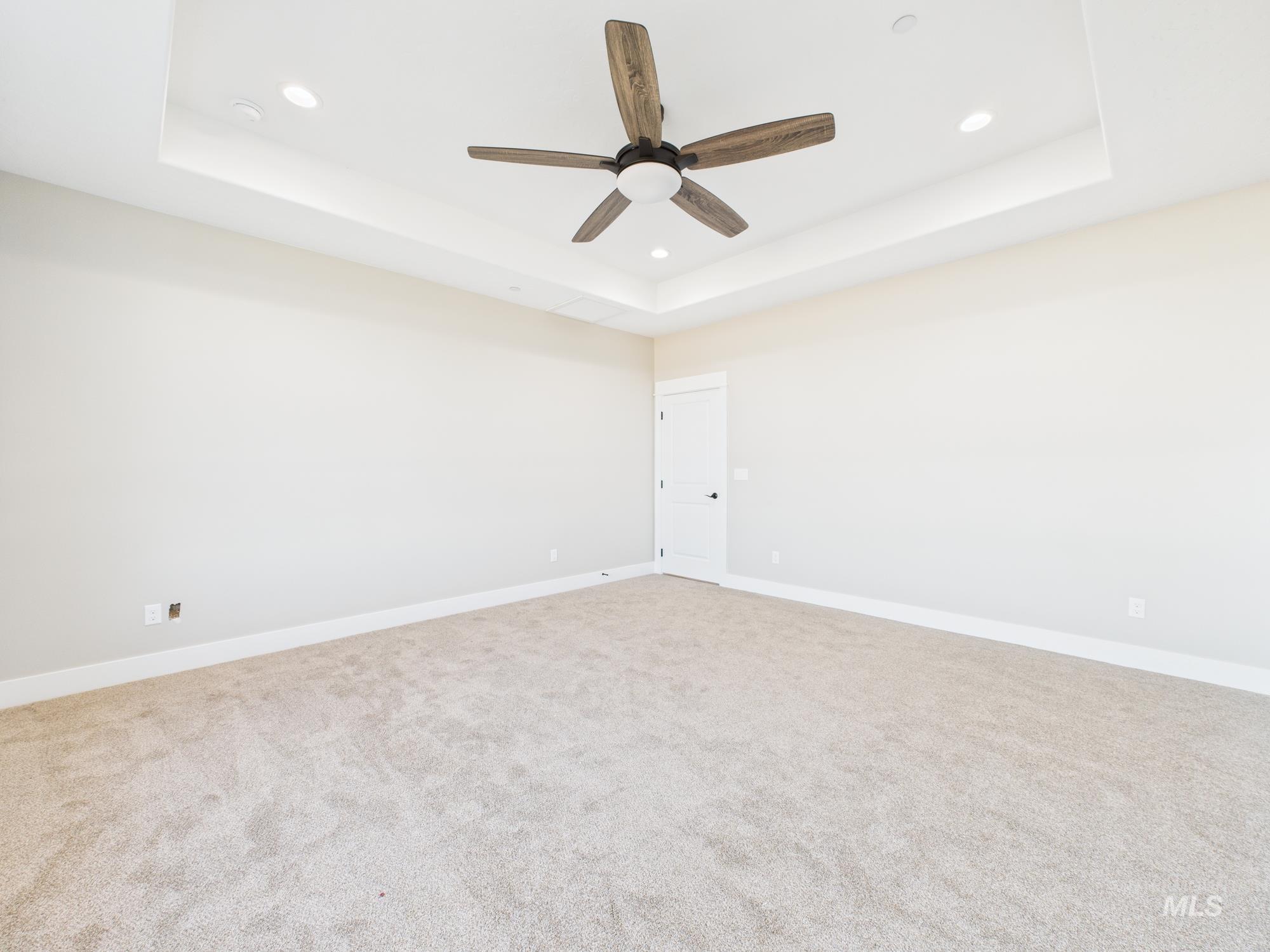 Empty room with a raised ceiling, light colored carpet, recessed lighting, and ceiling fan
