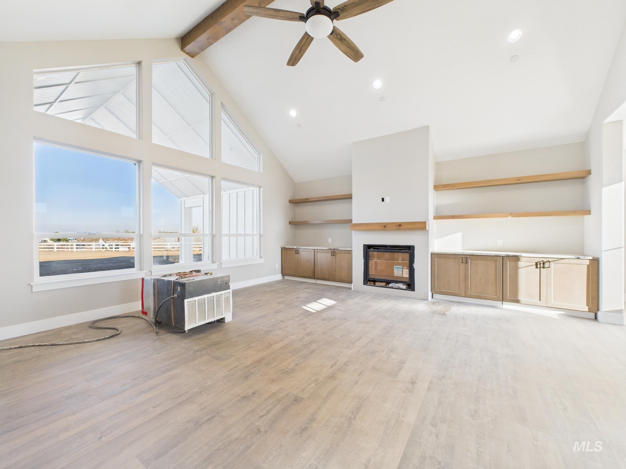 Unfurnished living room featuring light wood-style floors, high vaulted ceiling, ceiling fan, beam ceiling, and a fireplace