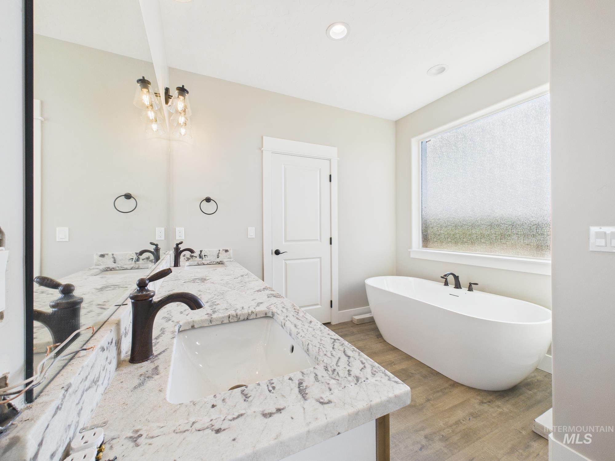 Bathroom with a freestanding tub, double vanity, light wood finished floors, and a chandelier