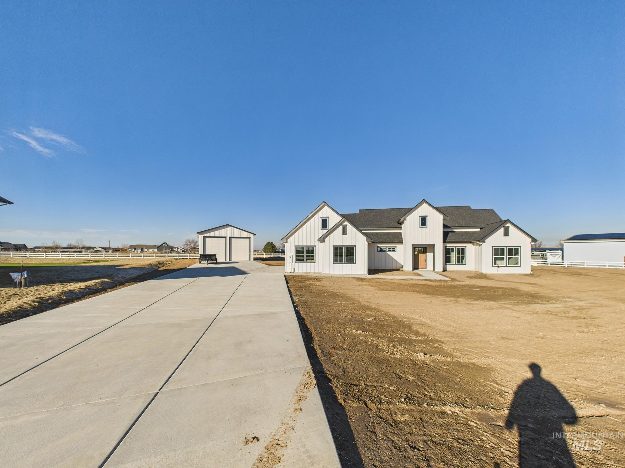 Modern farmhouse style home with a detached garage, an outbuilding, board and batten siding, and roof with shingles