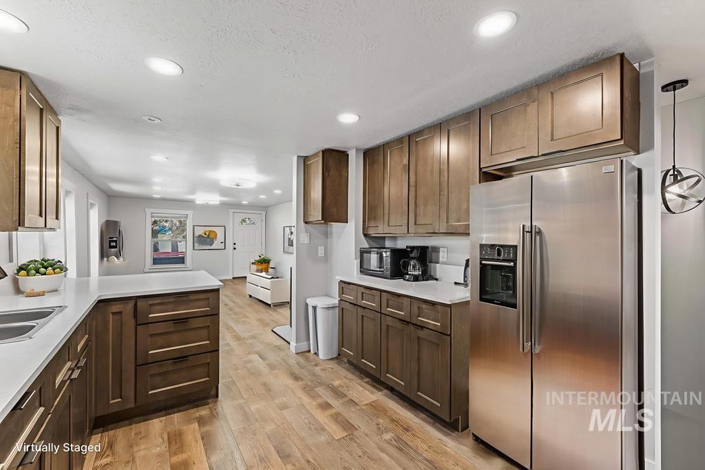Kitchen featuring stainless steel refrigerator with ice dispenser, recessed lighting, light wood-style floors, a peninsula, and decorative light fixtures