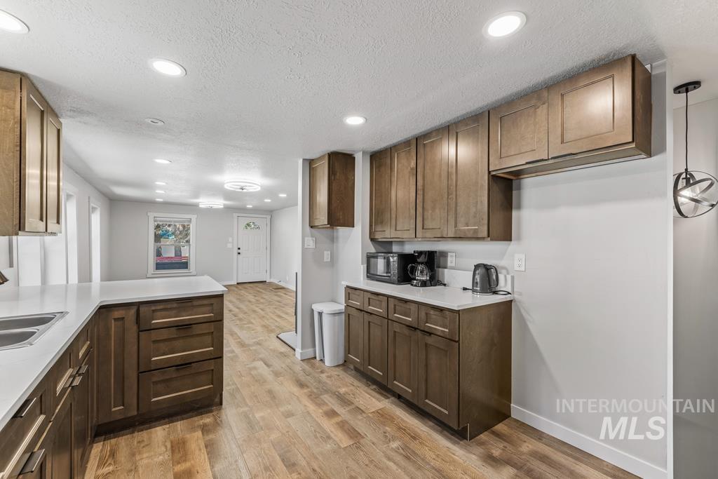 Kitchen with light wood-type flooring, recessed lighting, a peninsula, a textured ceiling, and pendant lighting