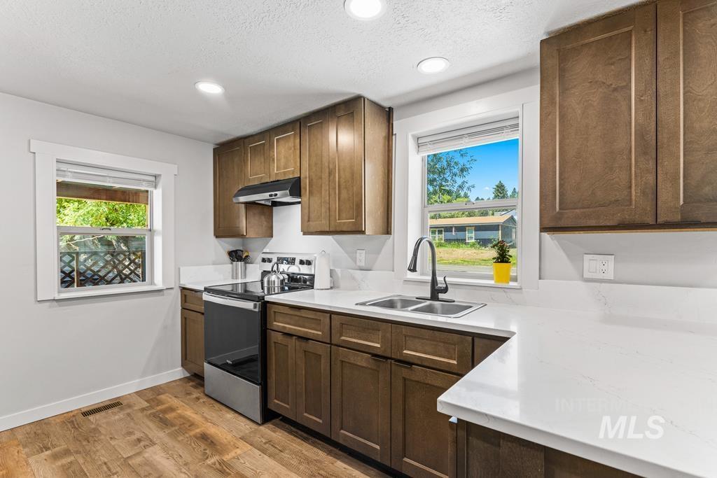 Kitchen with stainless steel electric range, light wood-type flooring, a textured ceiling, plenty of natural light, and recessed lighting