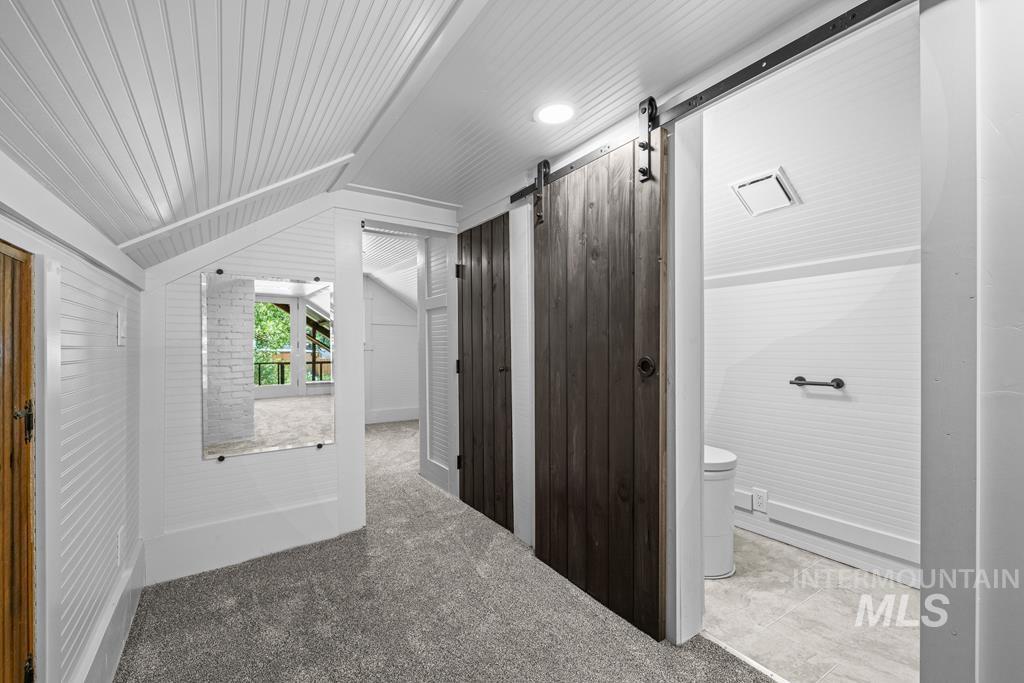 Additional living space with a barn door, carpet, and vaulted ceiling