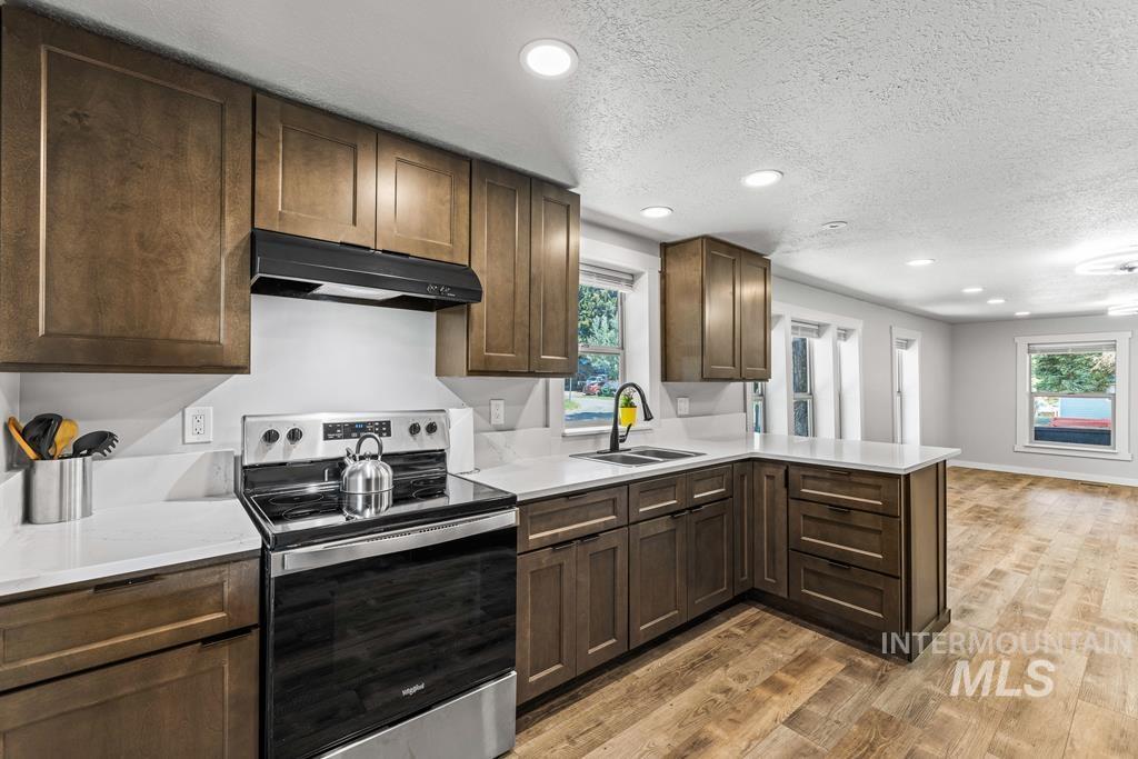 Kitchen with electric stove, dark brown cabinetry, recessed lighting, light wood-style floors, and under cabinet range hood