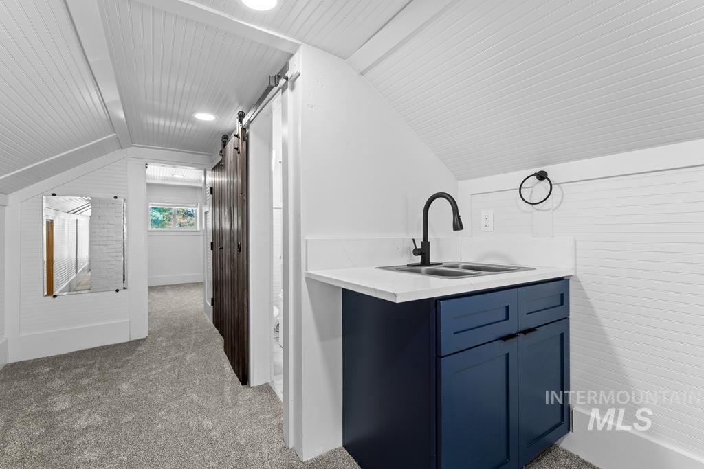 Bar area with blue cabinets, lofted ceiling, light carpet, and a barn door