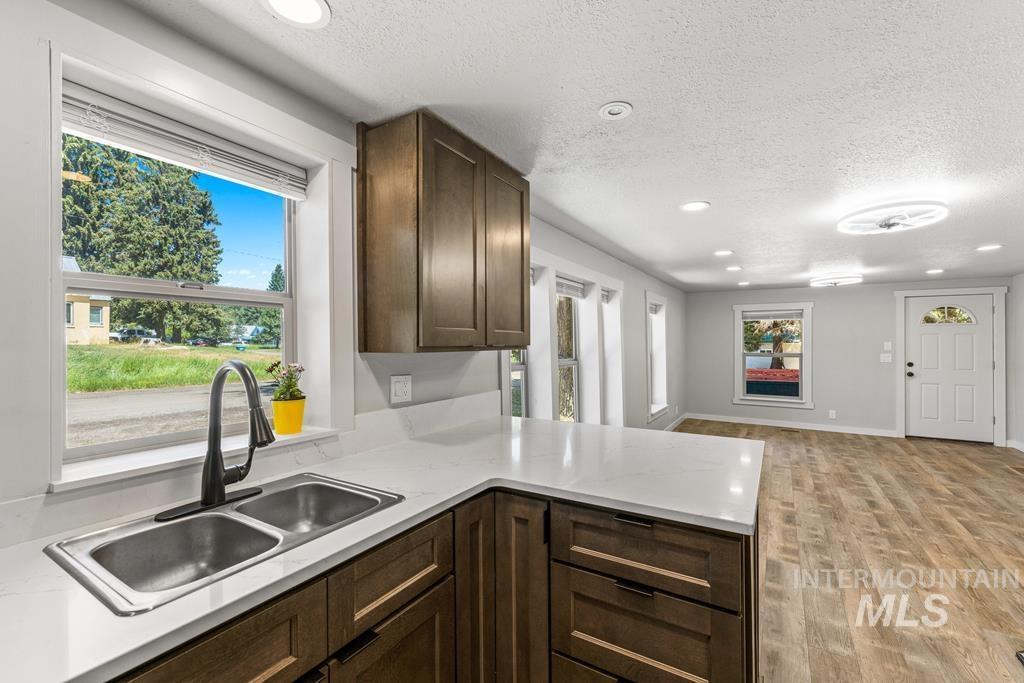Kitchen with dark brown cabinets, light wood-type flooring, recessed lighting, a textured ceiling, and light stone counters