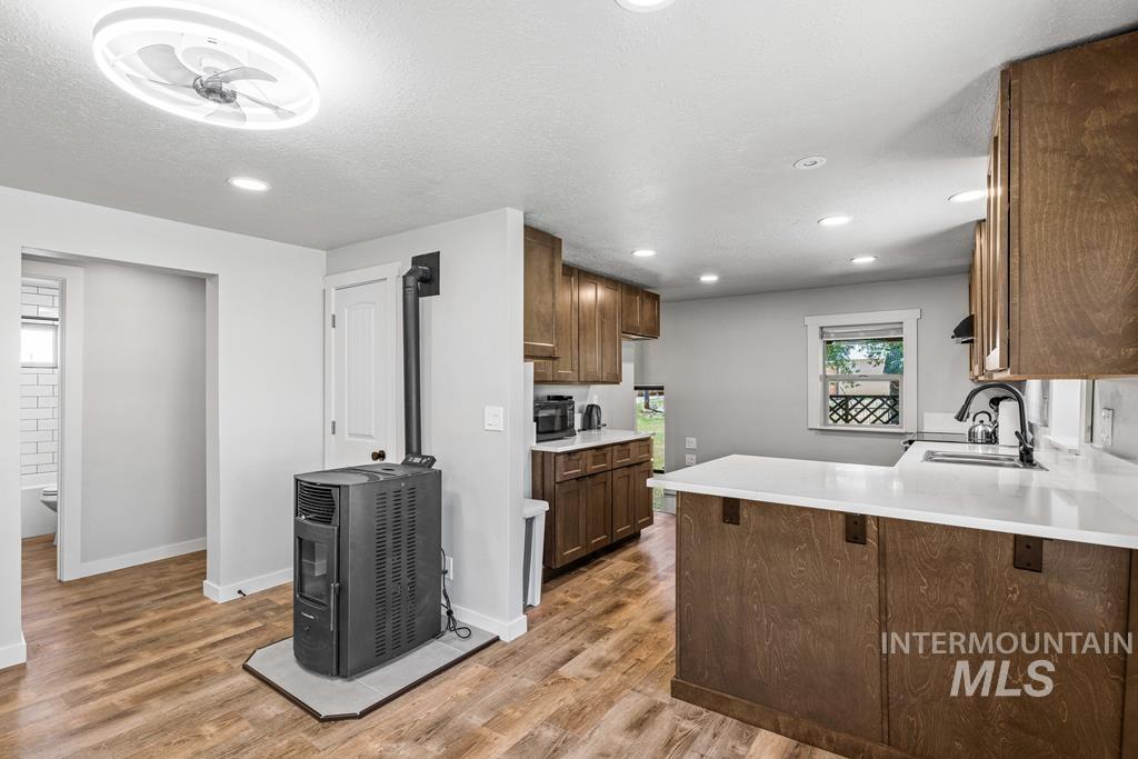 Kitchen featuring a peninsula, light wood finished floors, recessed lighting, light stone counters, and brown cabinetry