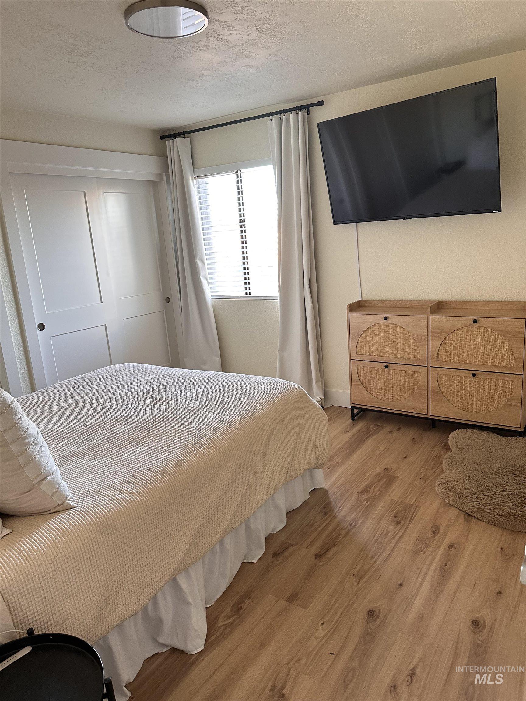 Bedroom with a textured ceiling, light wood finished floors, and a closet