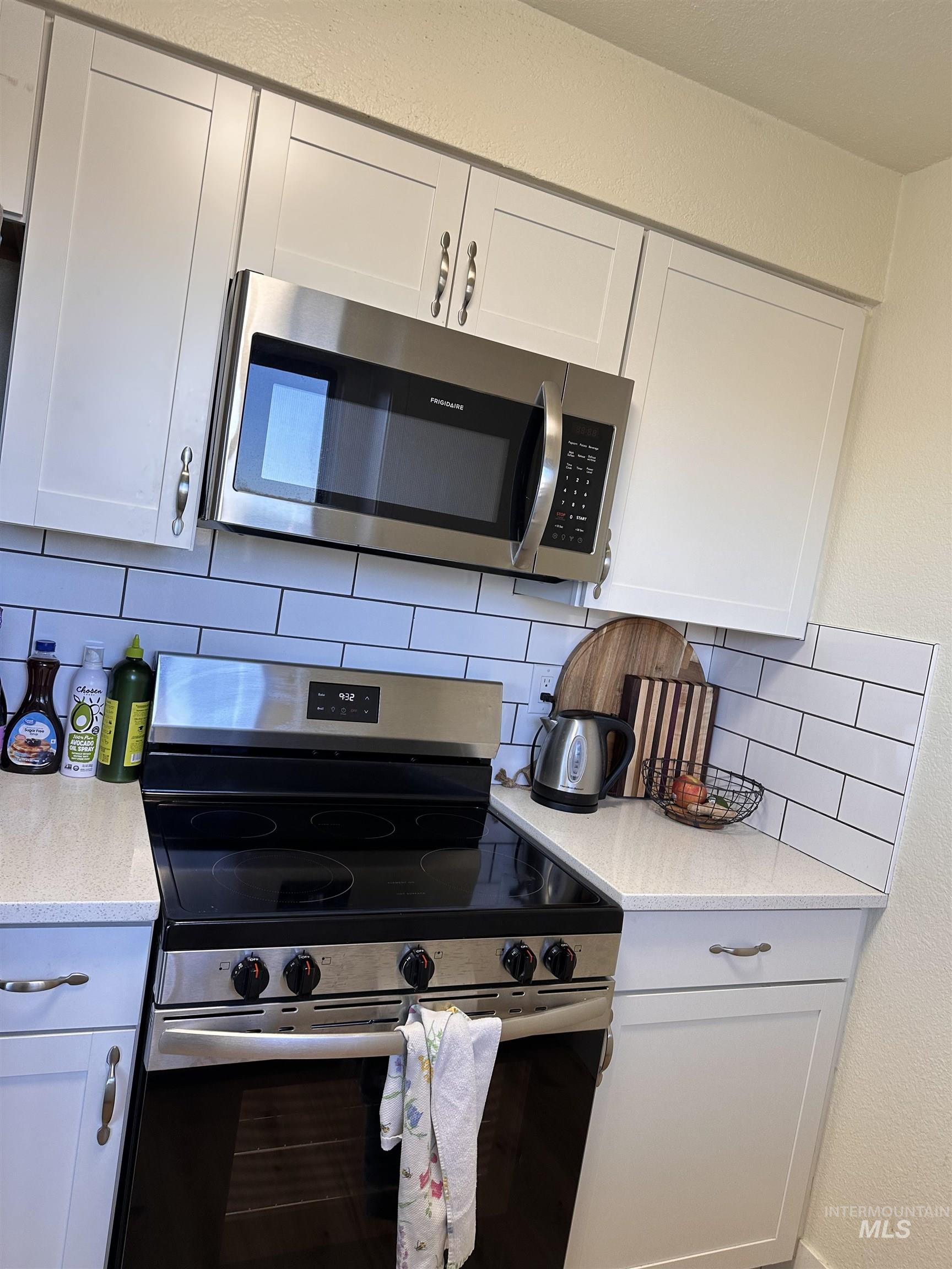 Kitchen with appliances with stainless steel finishes, a textured wall, white cabinets, light stone countertops, and backsplash