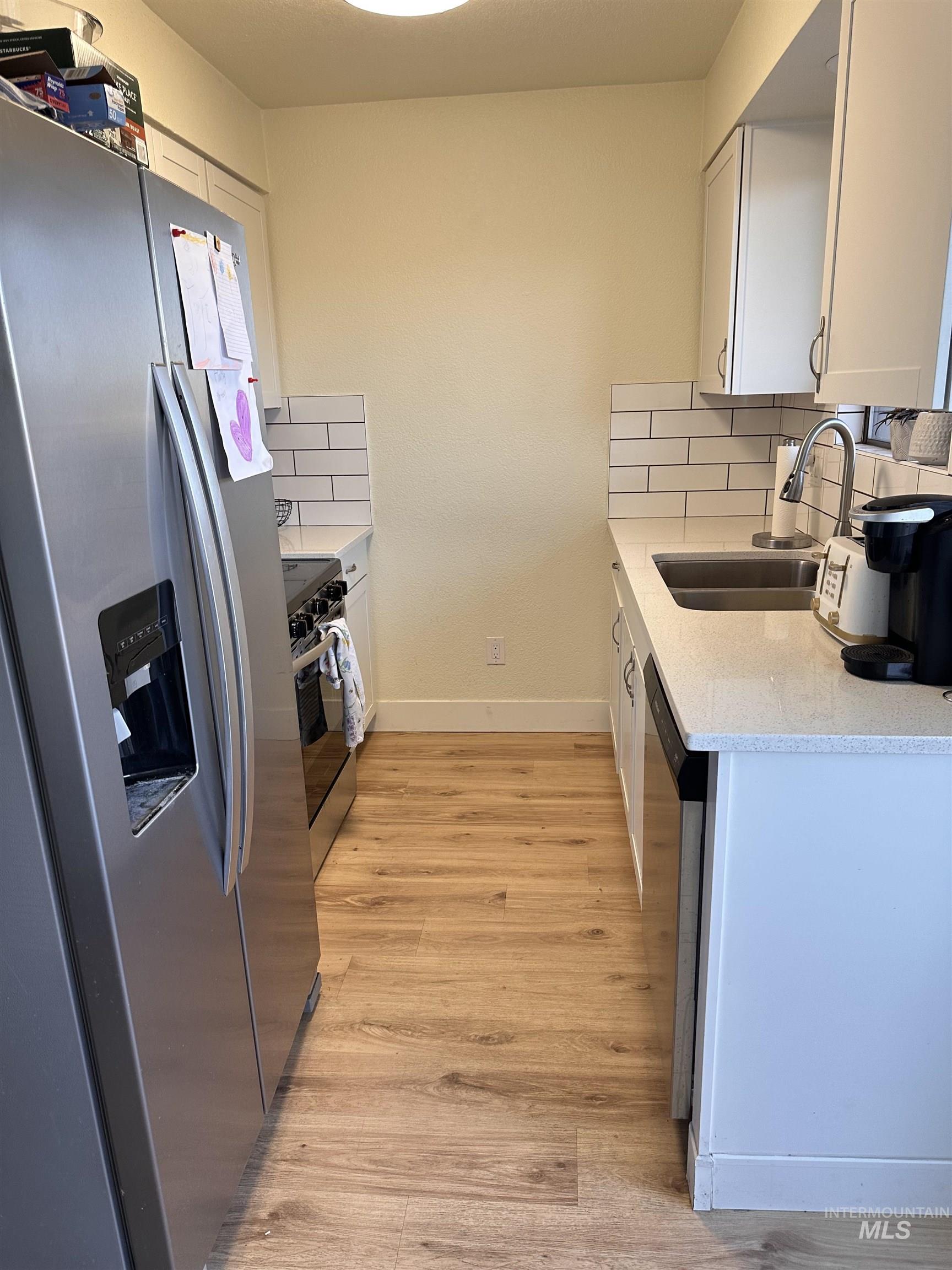 Kitchen featuring appliances with stainless steel finishes, white cabinetry, light stone counters, light wood-style floors, and decorative backsplash