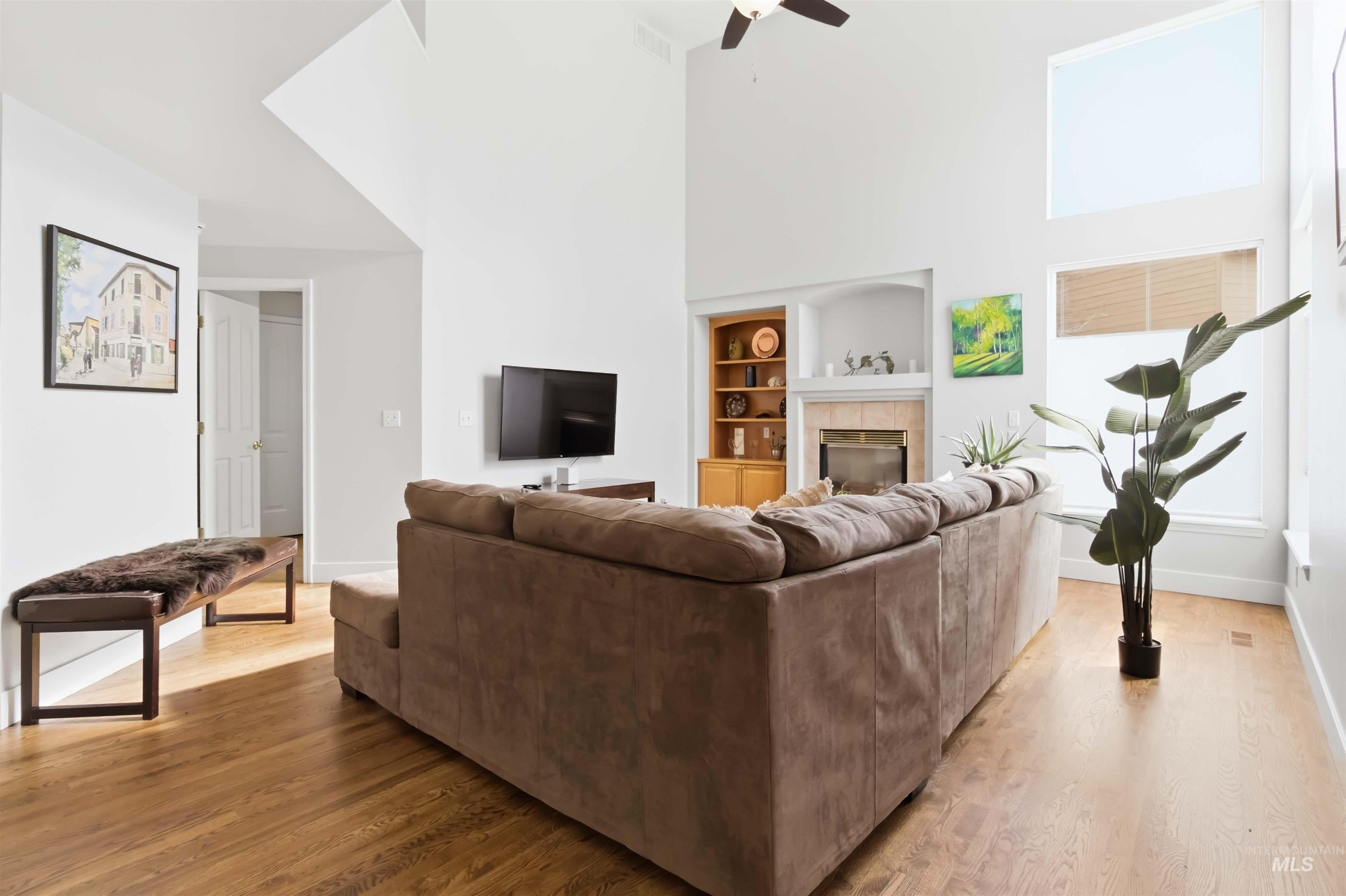 Living room with built in shelves, a high ceiling, light wood finished floors, a ceiling fan, and a fireplace
