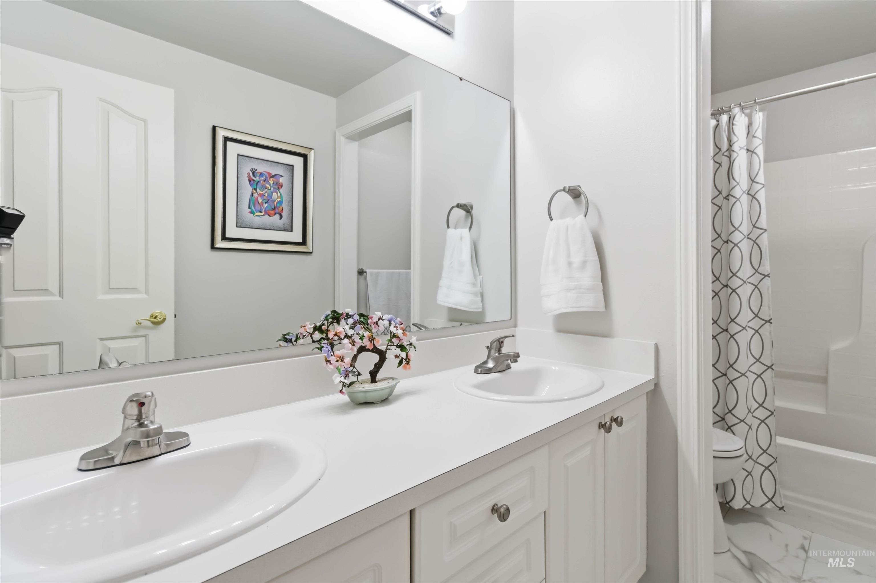 Bathroom with double vanity, shower / bathtub combination with curtain, and marble look tile flooring