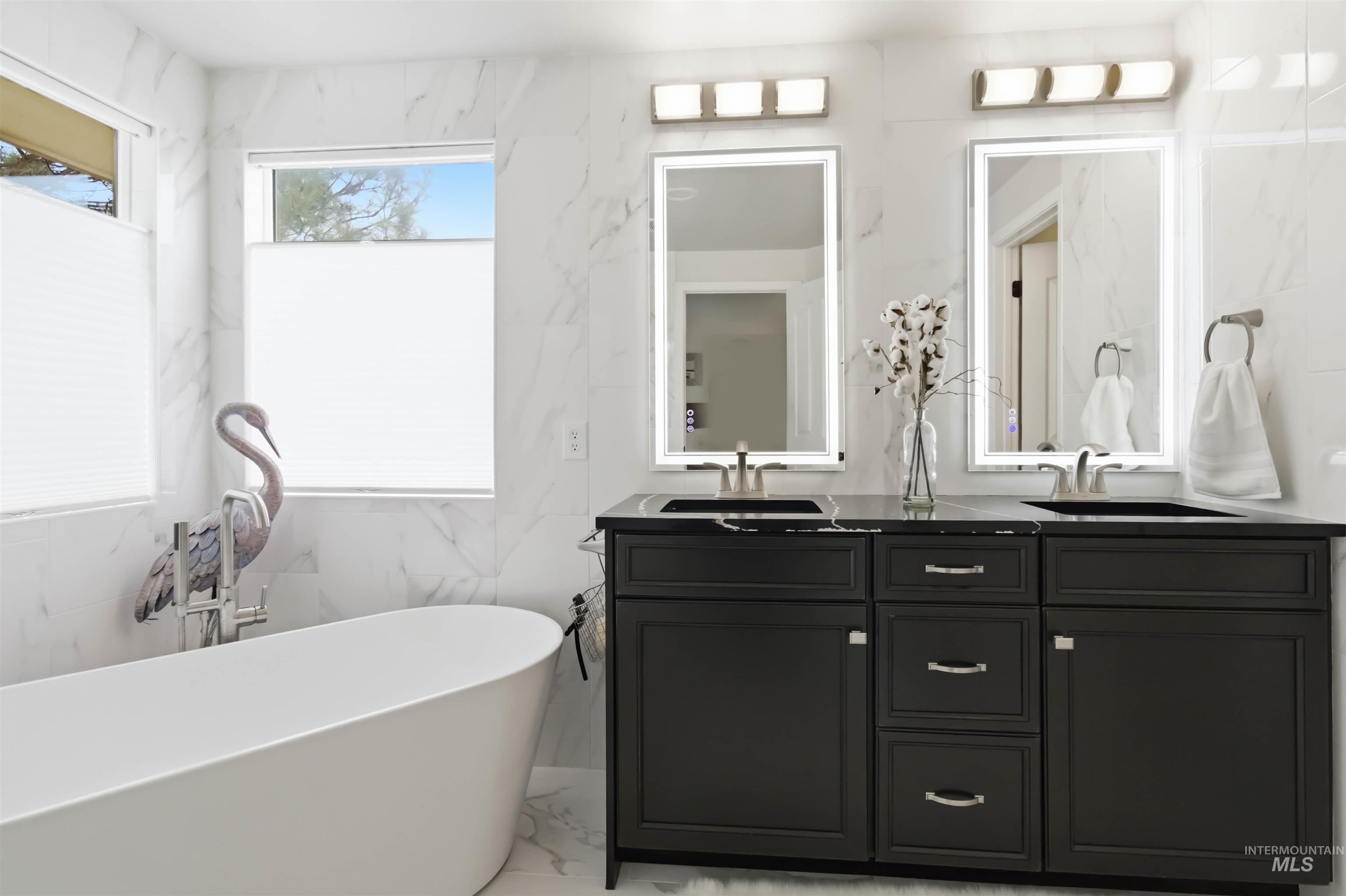 Bathroom with double vanity, stone wall, a soaking tub, and light marble finish flooring