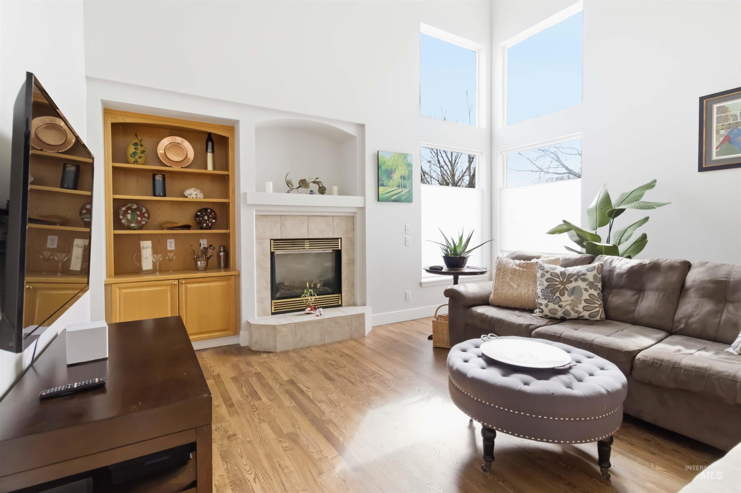 Living area with a high ceiling, light wood-type flooring, a fireplace, and built in shelves
