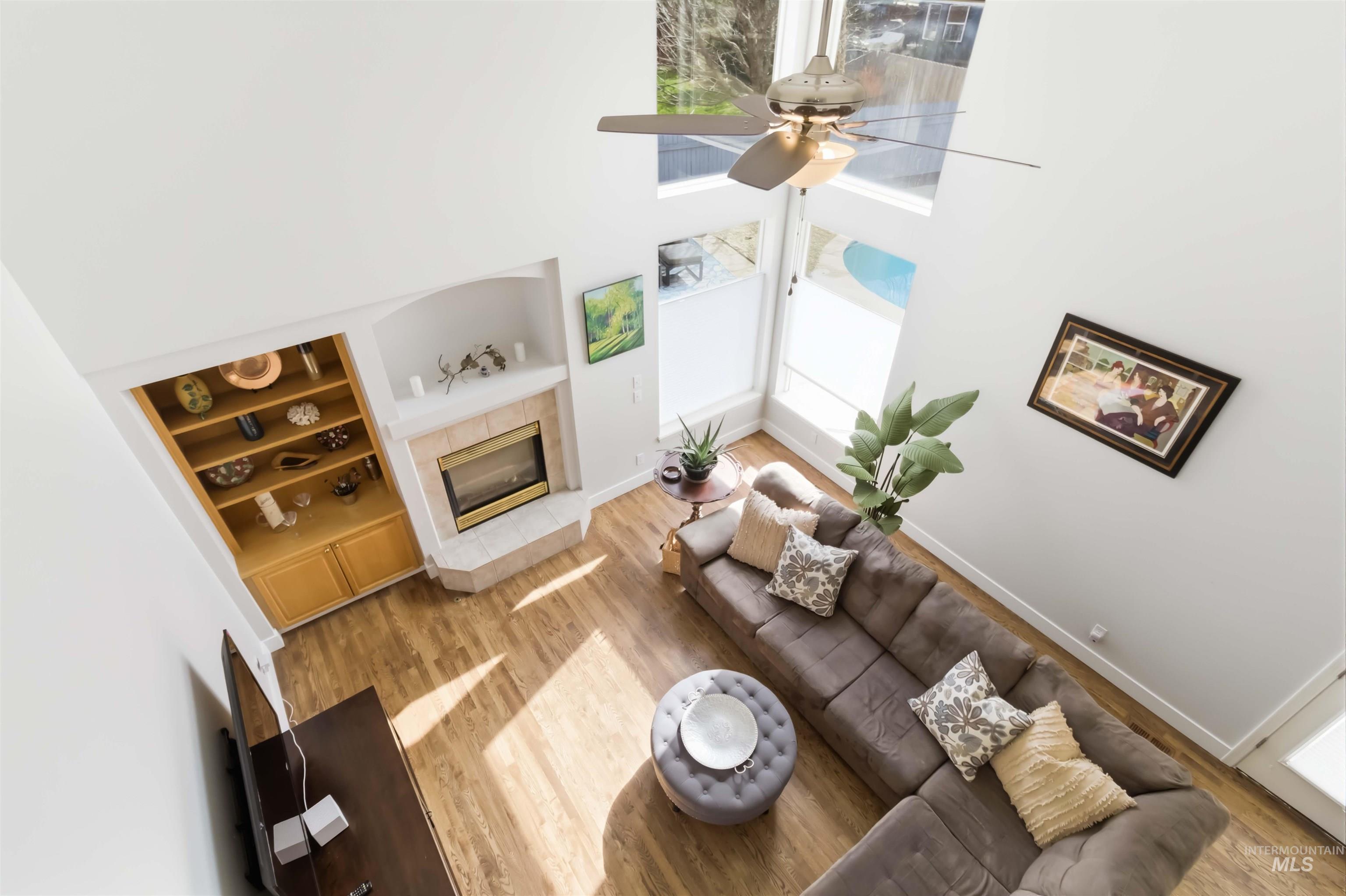 Living area featuring built in shelves, a high ceiling, light wood-style flooring, a fireplace, and a ceiling fan