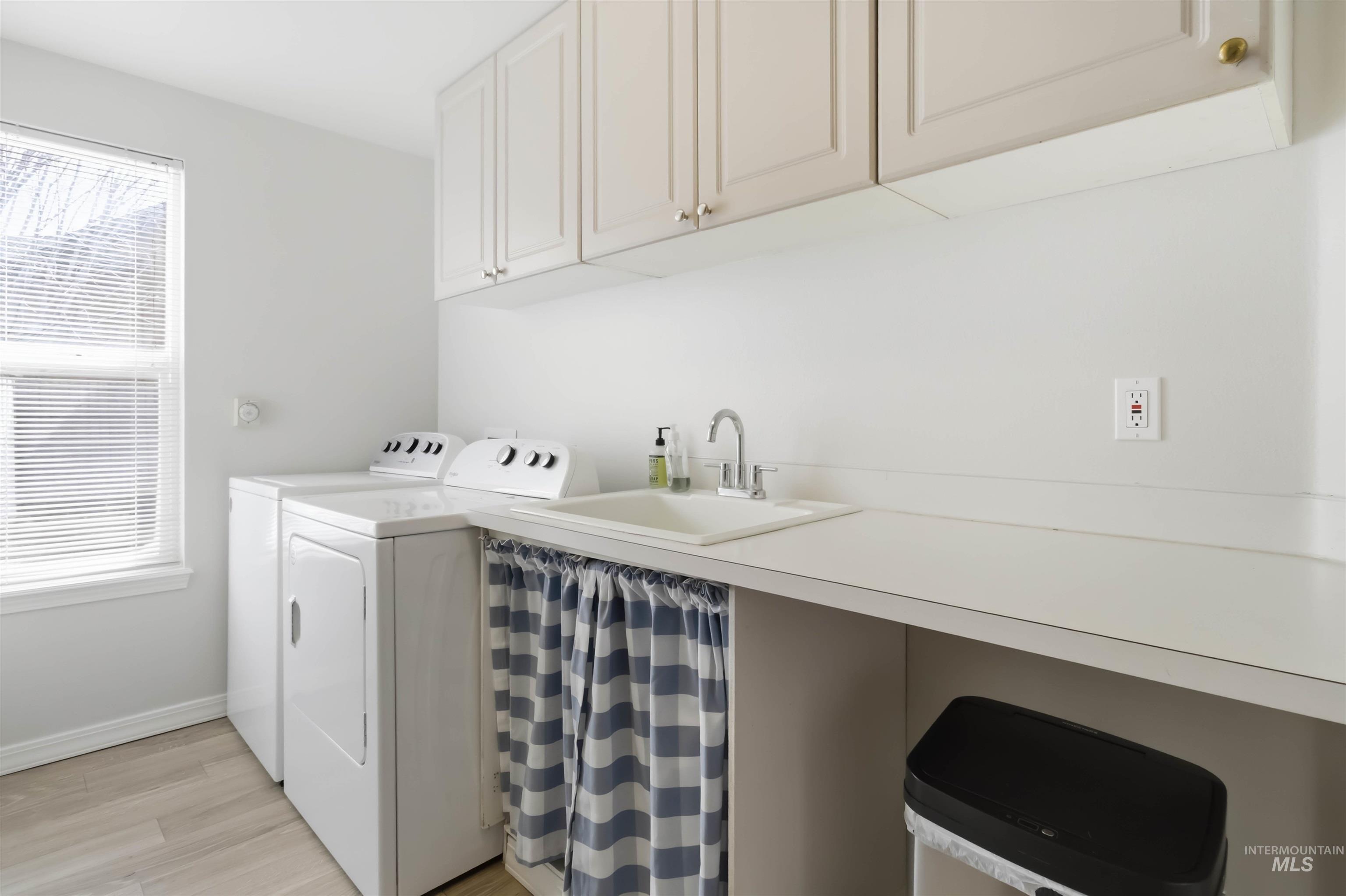 Laundry room with washer and dryer, light wood-type flooring, and cabinet space
