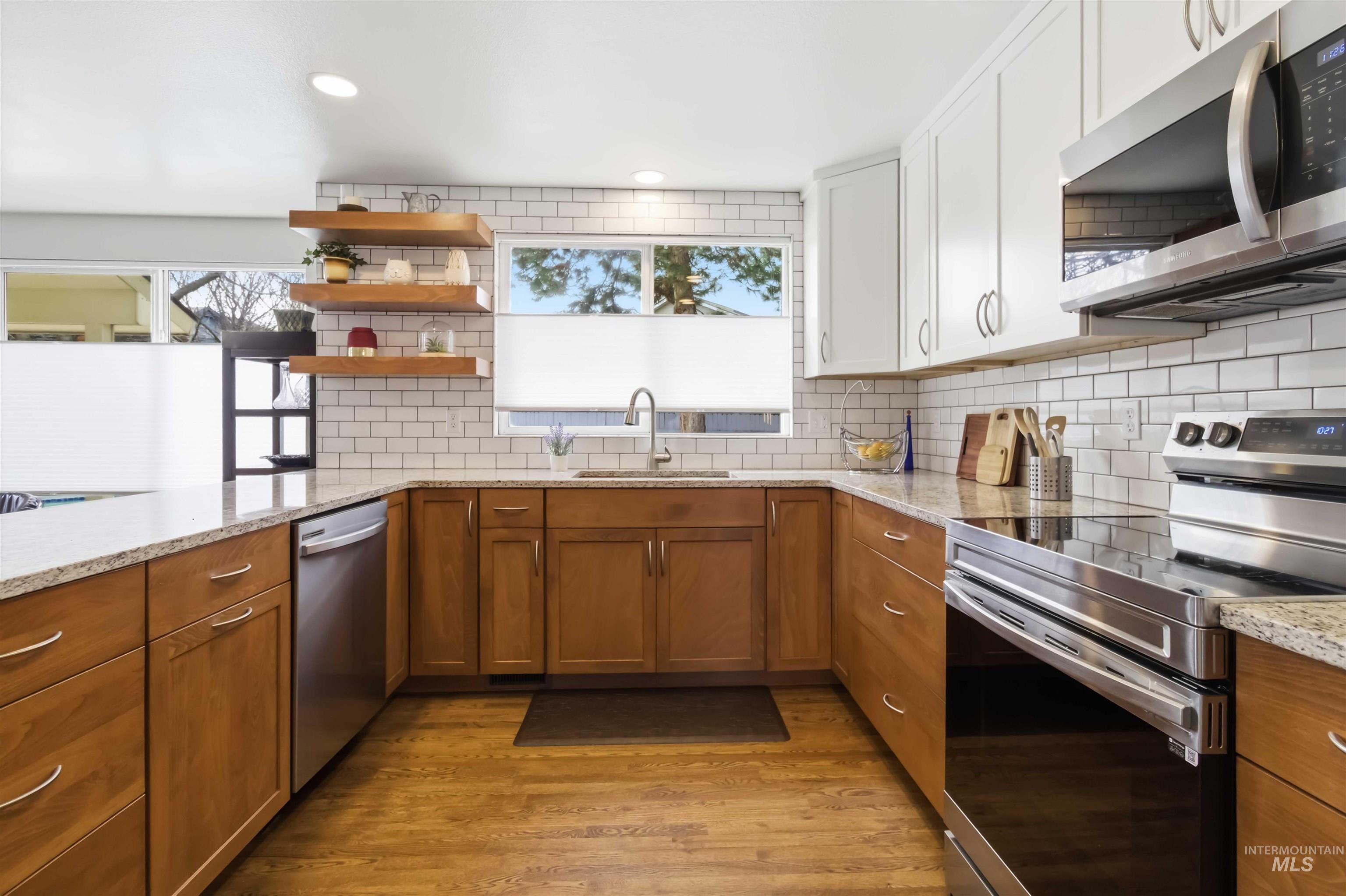 Kitchen with stainless steel appliances, wood finish cabinets, light stone countertops, open shelves, and light wood-style floors