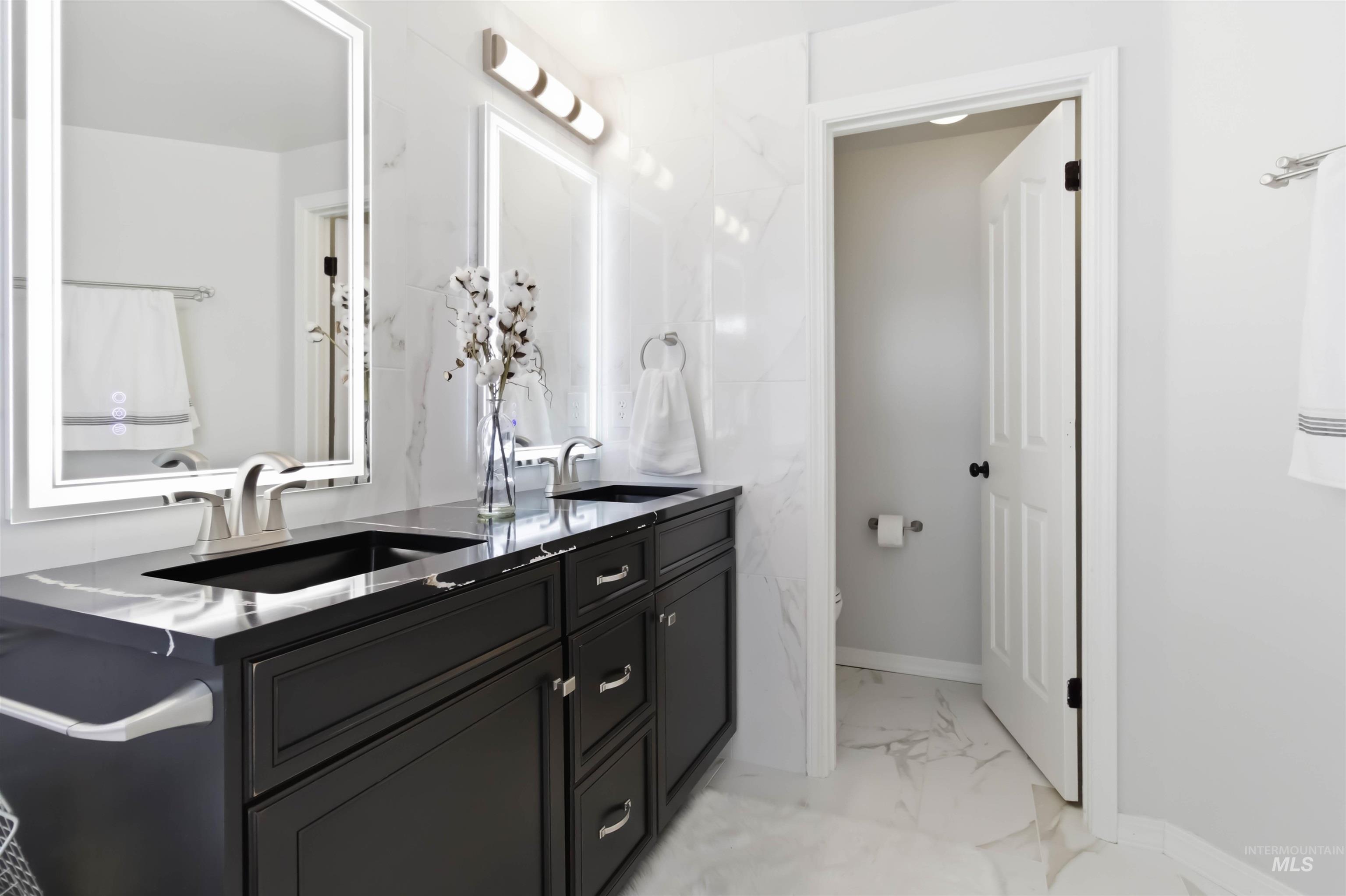 Full bath featuring double vanity and light marble finish floors