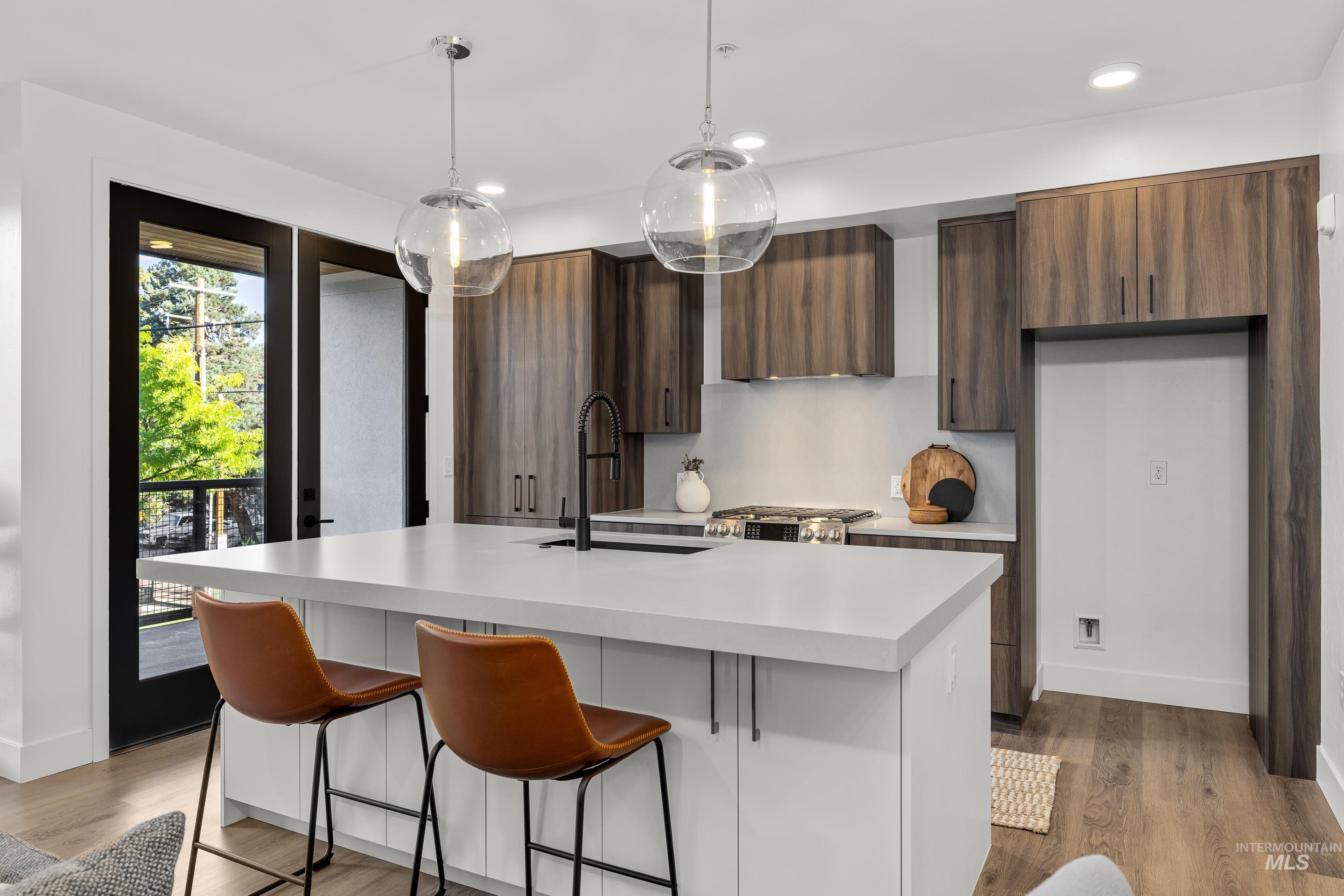 Kitchen featuring a kitchen bar, modern cabinets, light wood-style floors, decorative light fixtures, and a center island with sink