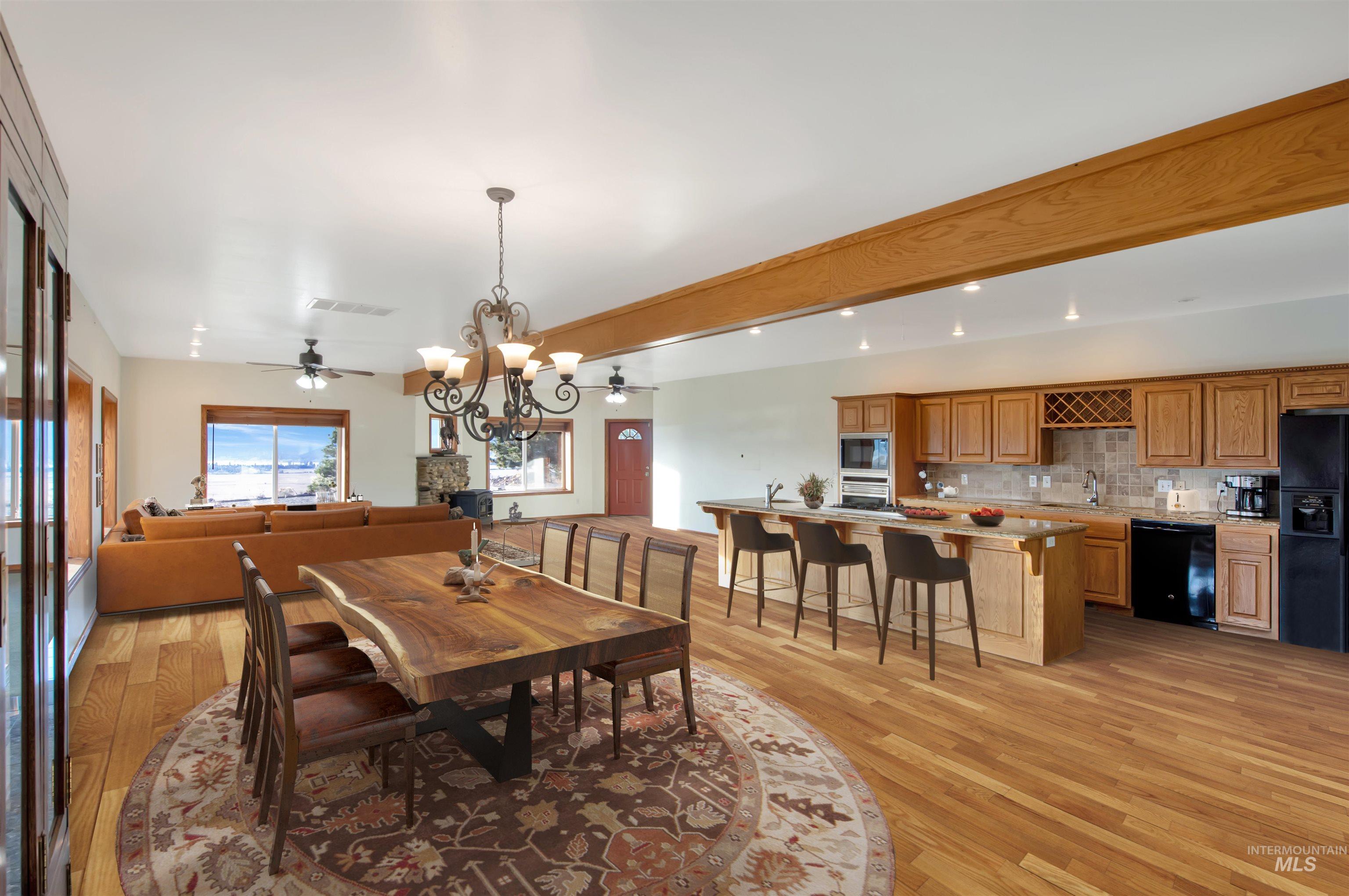 Dining space featuring a chandelier, beamed ceiling, light wood-style flooring, and ceiling fan. Note that home is vacant and has been virtually staged for the purpose of this photo.