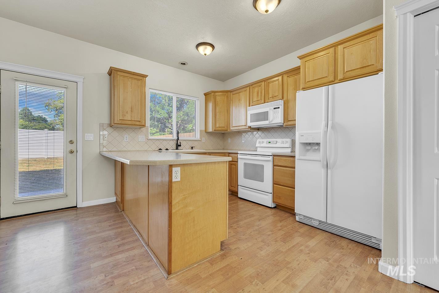 Kitchen with white appliances, a peninsula, backsplash, and light wood finished floors