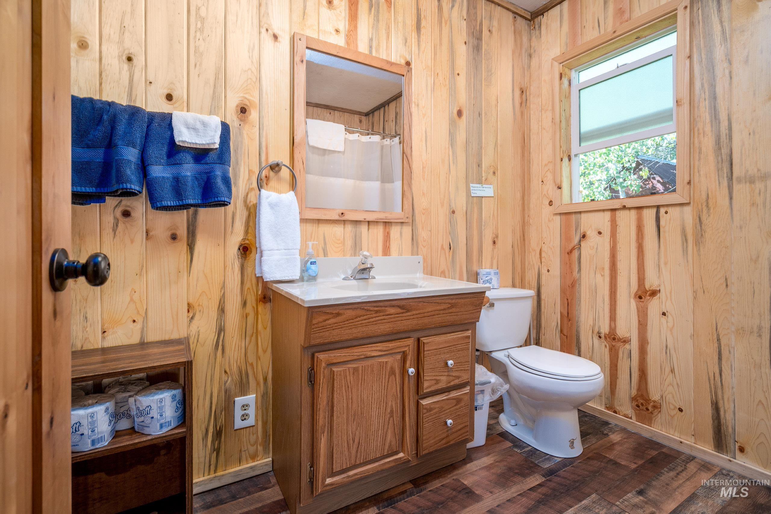 Full bathroom with wooden walls, curtained shower, dark wood finished floors, and vanity