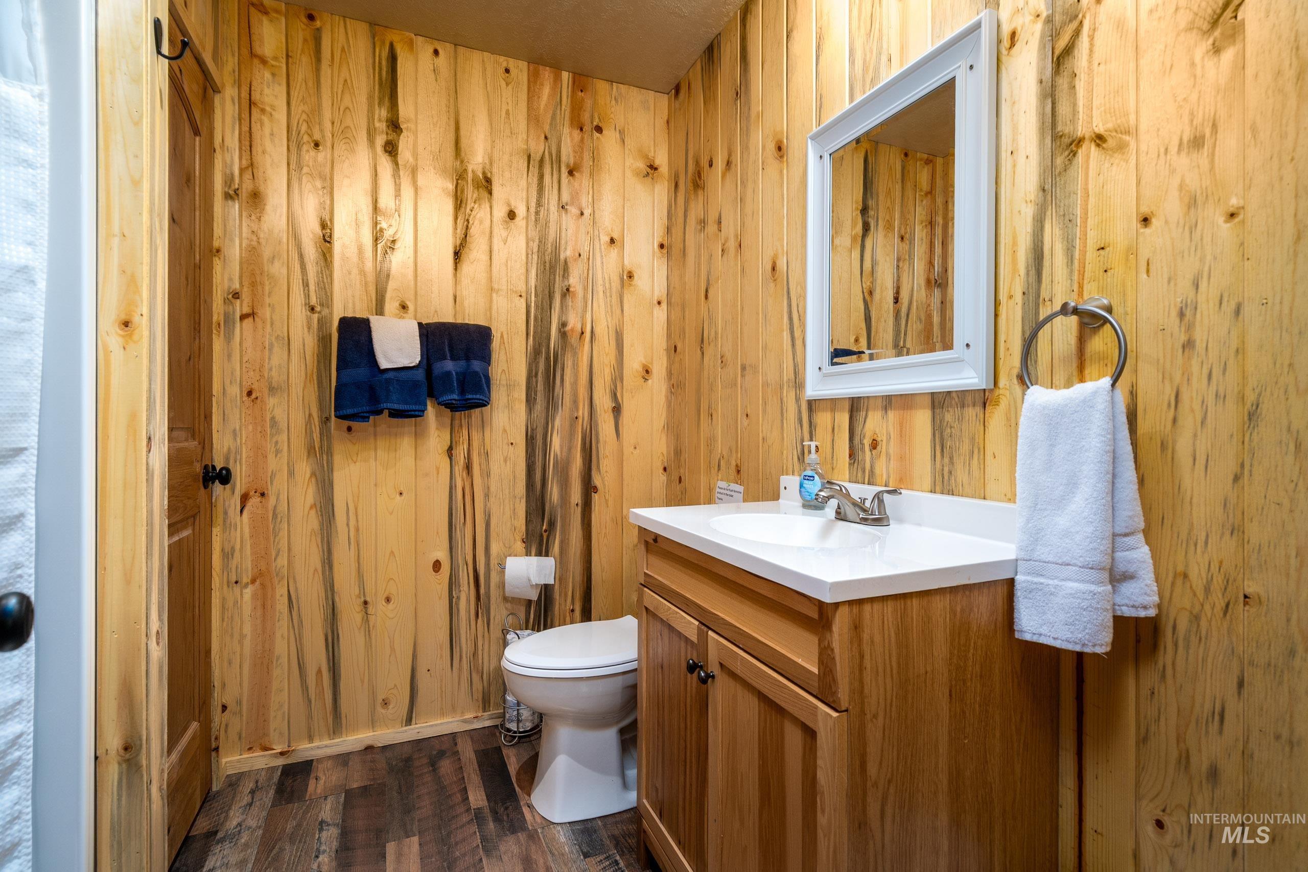 Half bathroom featuring vanity, dark wood-style flooring, and wood walls