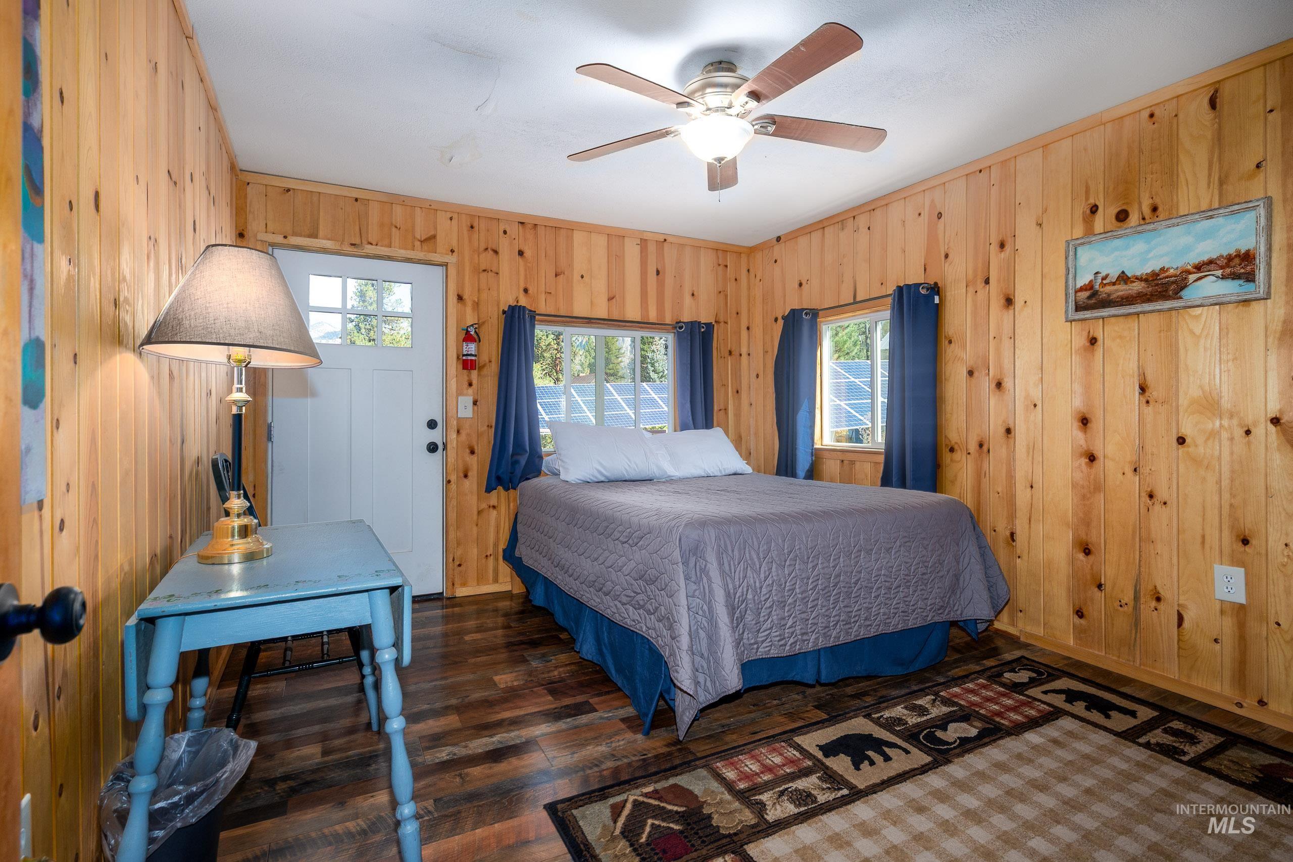 Bedroom featuring dark wood-type flooring, wooden walls, ceiling fan, and ornamental molding