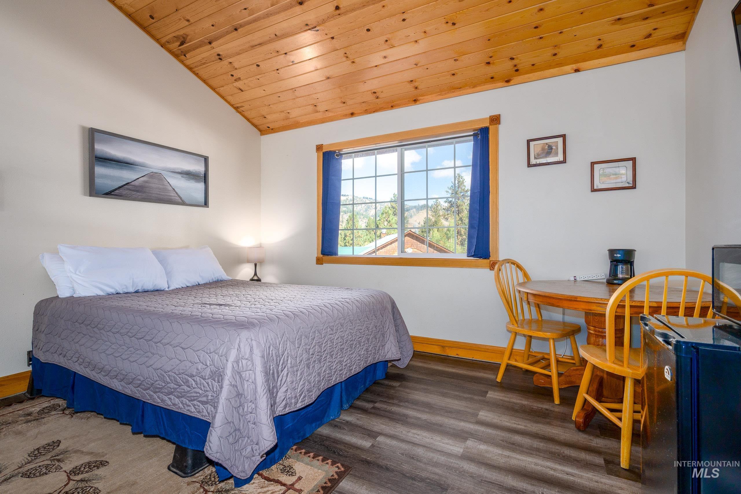 Bedroom with vaulted ceiling, wooden ceiling, wood finished floors, and black refrigerator