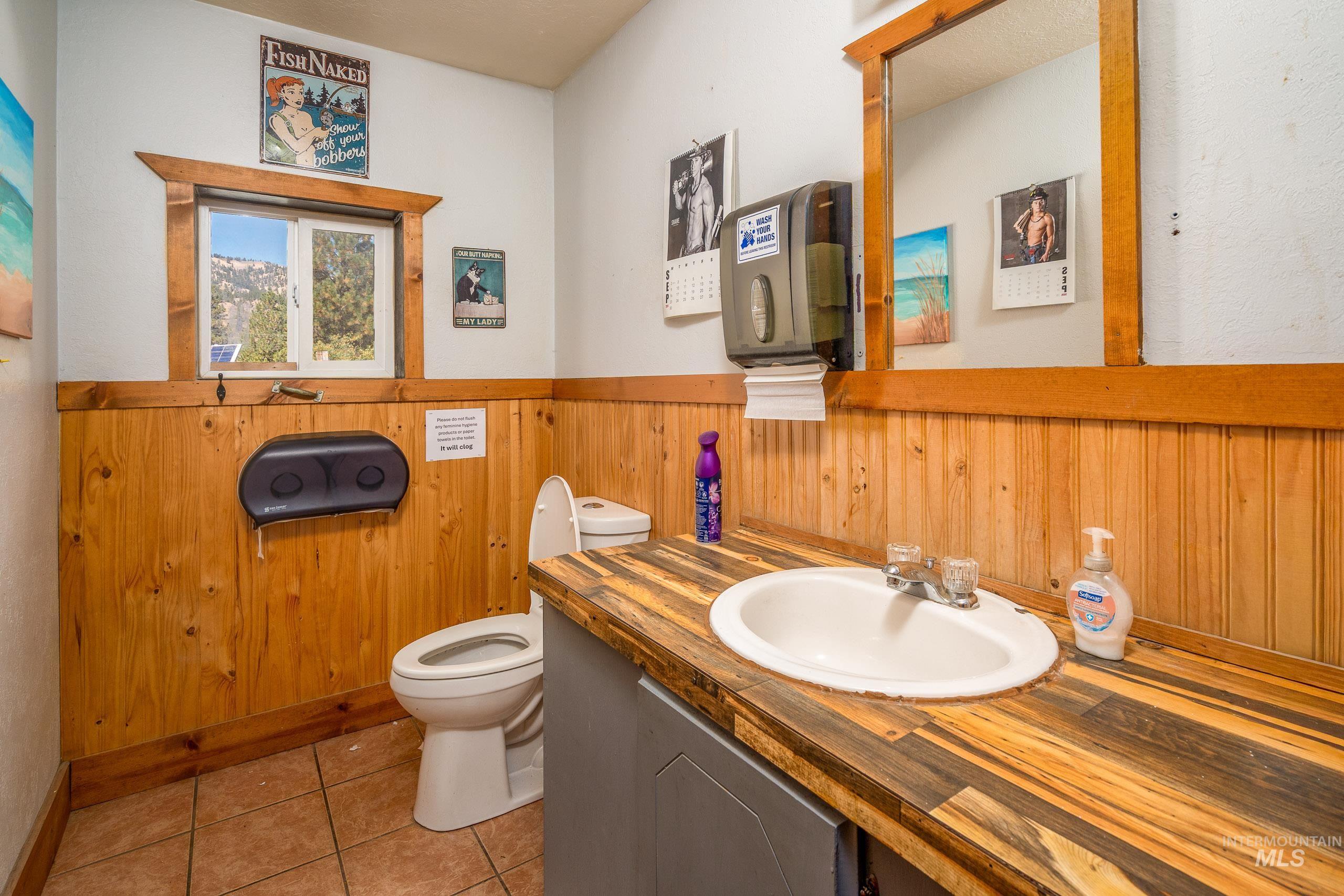 Bathroom with wood walls, light tile patterned floors, wainscoting, and vanity